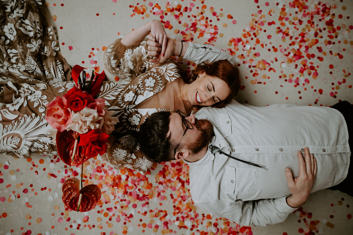 Vegas wedding couple lay in pink and red confetti.