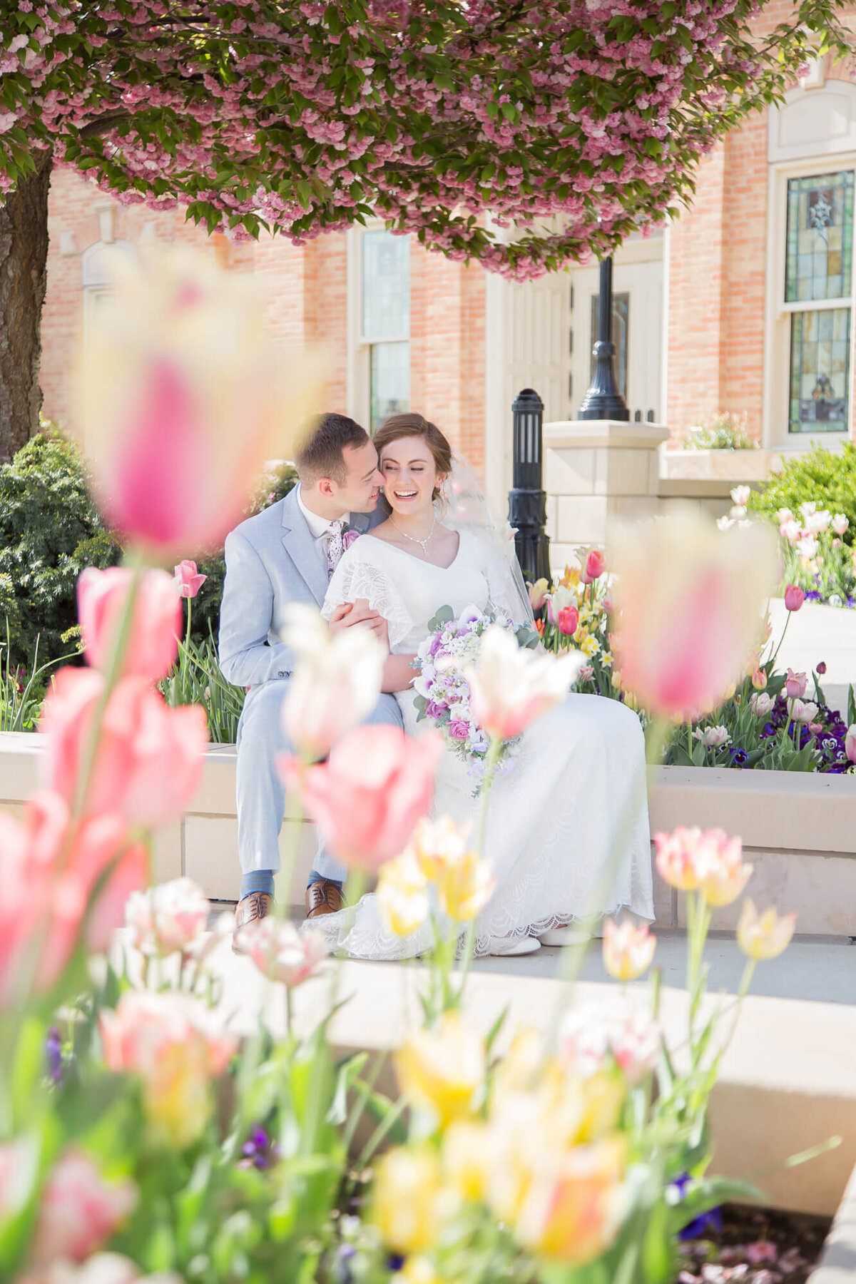 groom kissing bride's cheek while sitting in a tulip garden