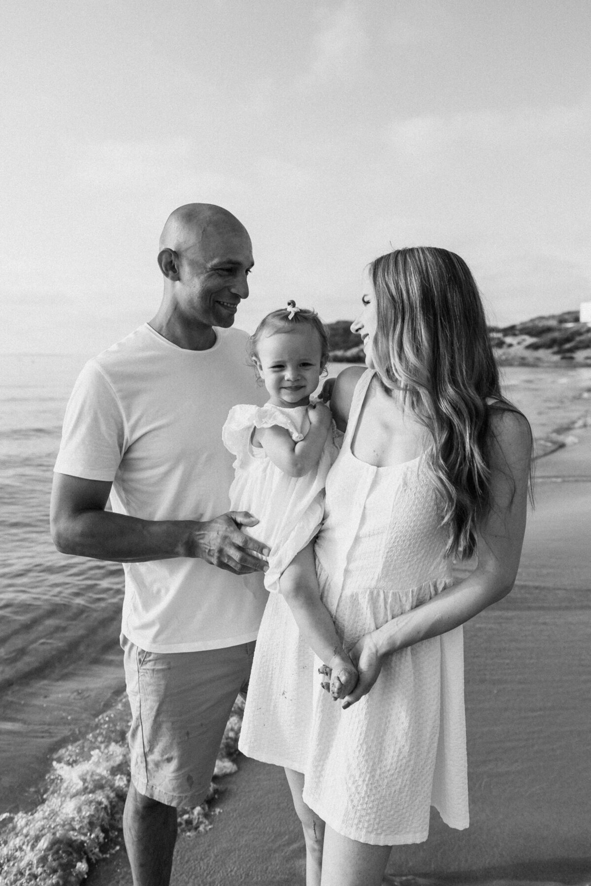 Woman is holding her daughter and looking lovingly at her man for a family photoshoot on Ibiza