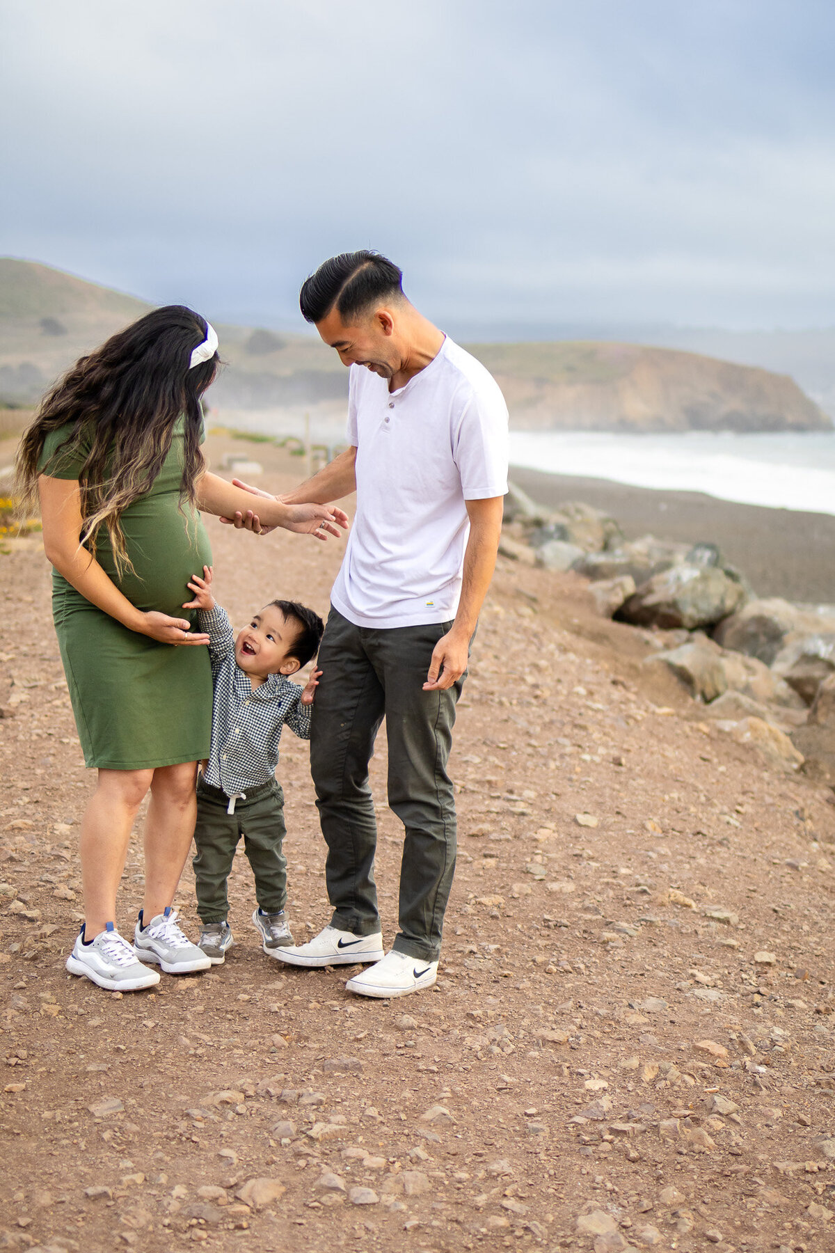 ighthearted moment of pregnant mom, dad, and toddler laughing together on a scenic coastal path, Bay Area Maternity Portfolio - Ellobelle Photography