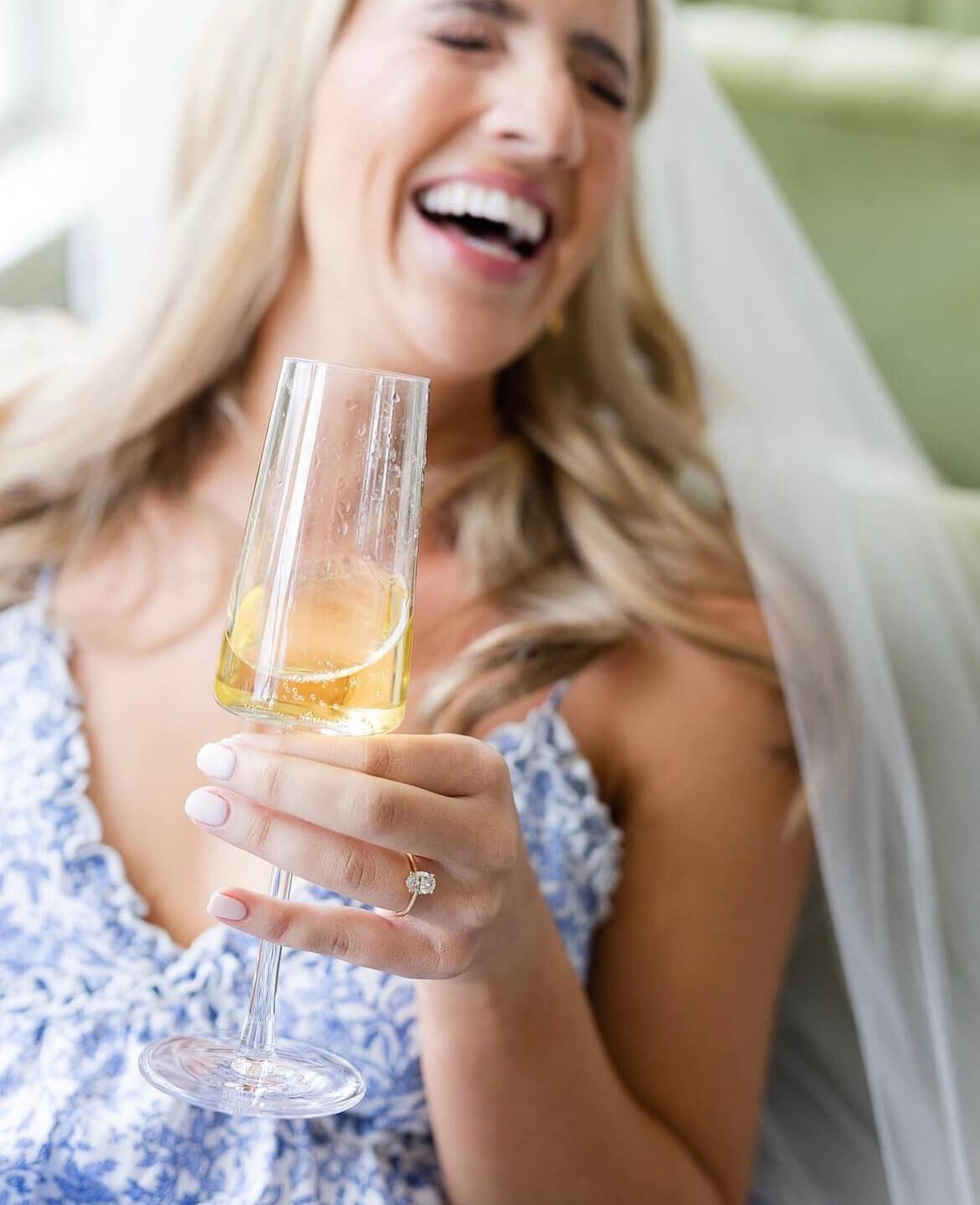 Bride laughing with champagne glass, showing off soft white bridal manicure and natural curls | Austin wedding nails and hair stylist