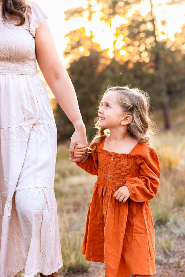 A little girl holds her moms hand and looks up at her.