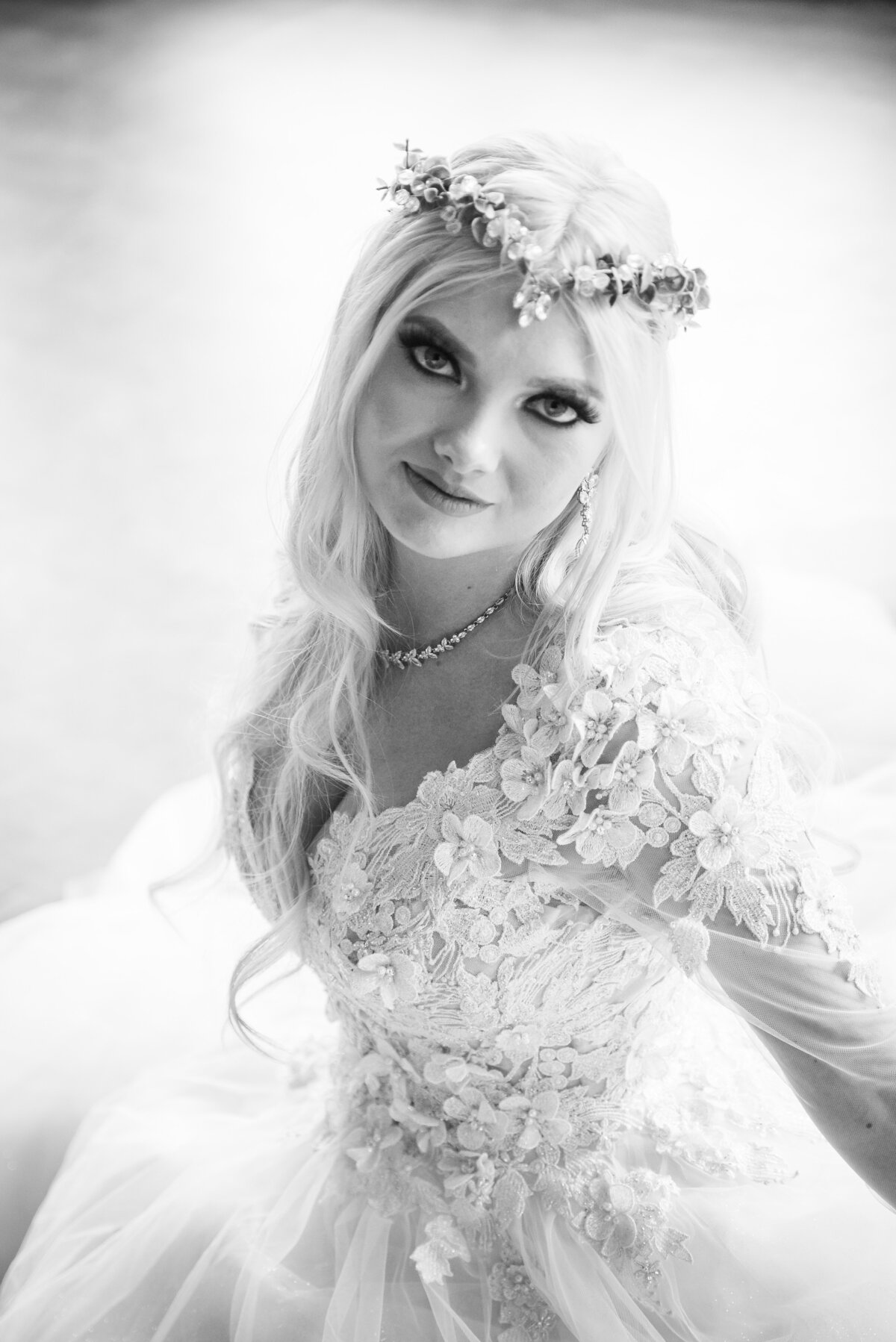 A bride wearing a long sleeve dress and intricate headpiece stares at the camera with a soft smile.