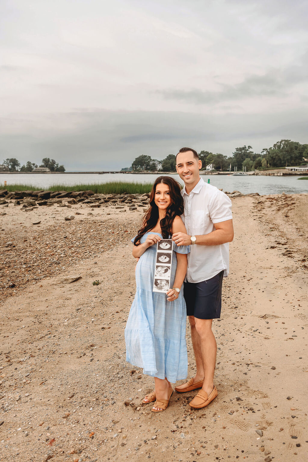 Connecticut maternity photographer documents couple holding ultrasound photos at beach session