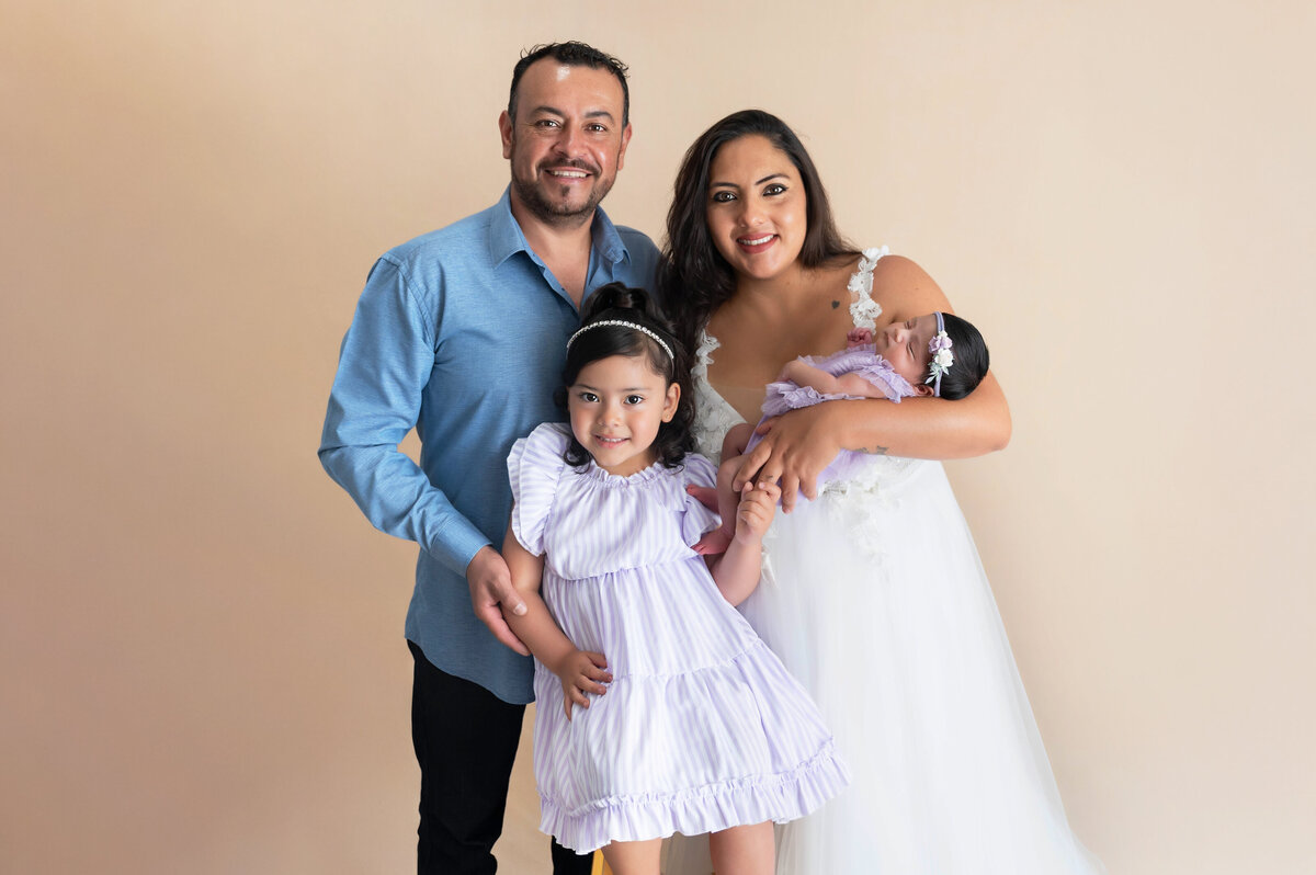 Family of four dressed in coordinating formal attire snuggled close for a close up family portrait.