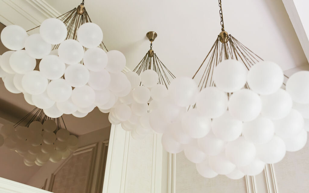 Three modern chandeliers with frosted white glass globes hang from the ceiling of a room with light-colored walls.