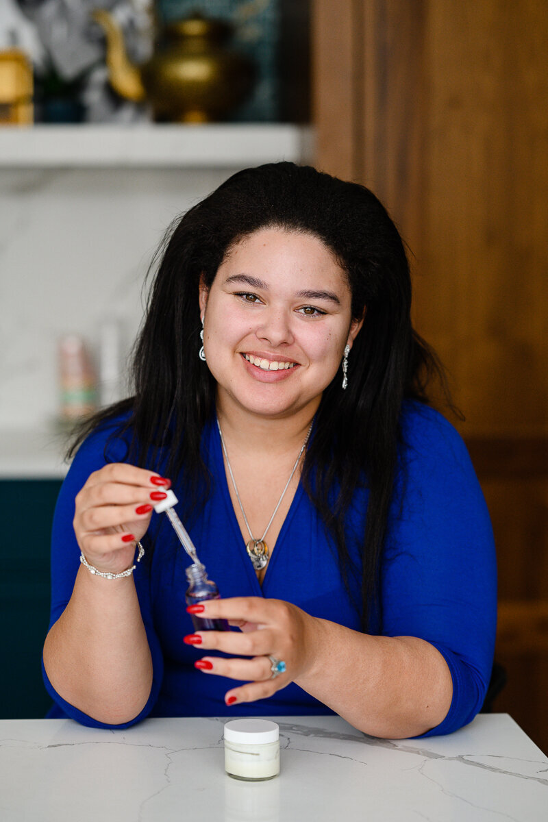 A woman in a blue dress holds a bottle of beauty products while smiling at a brand photographer in Denver for a  brand photography in denver.