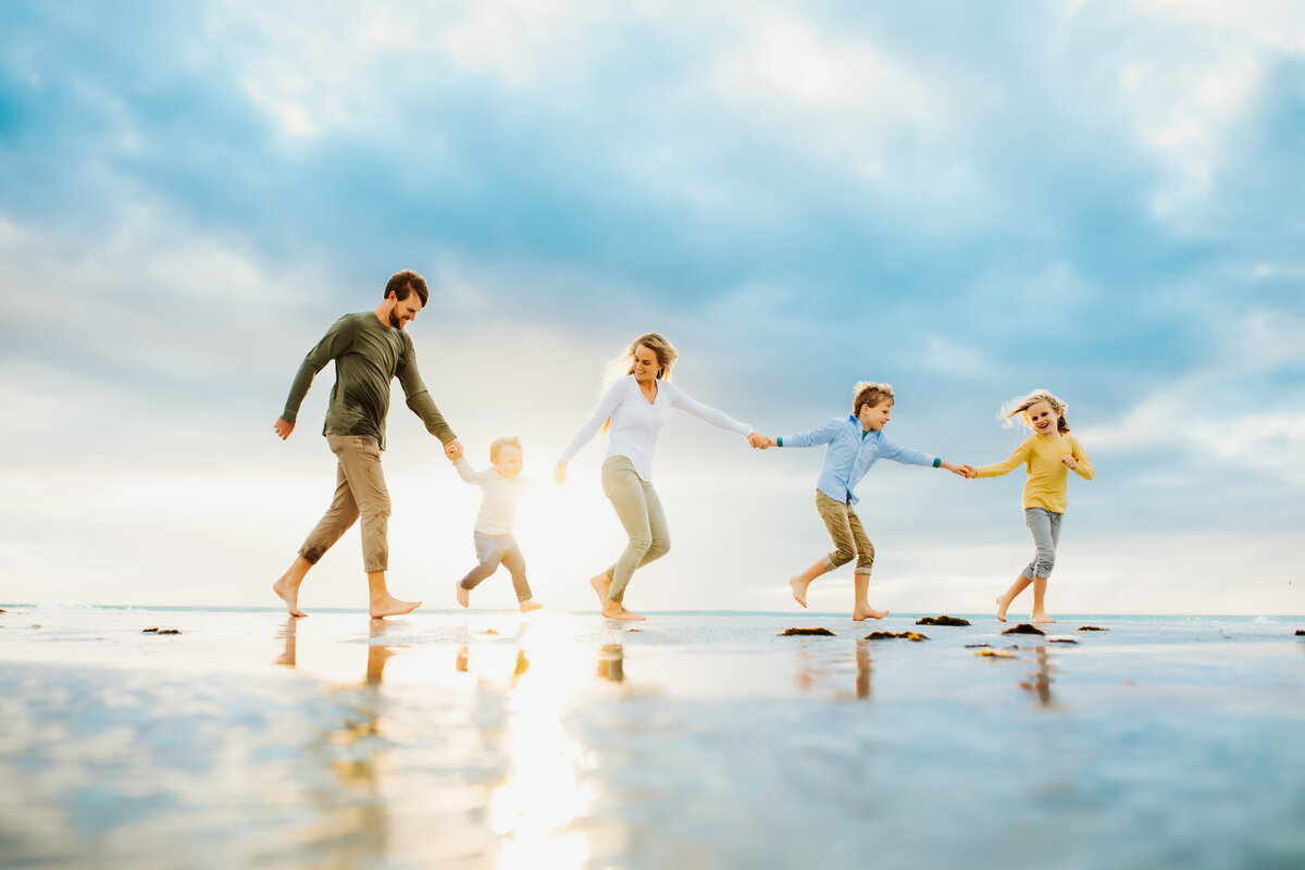 a large family having fun at sunset on the beach holding hands running in the water together