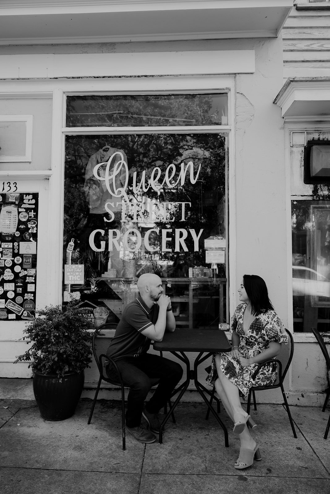 Couple sitting at table outside with Queen Street Grocery written on window in background