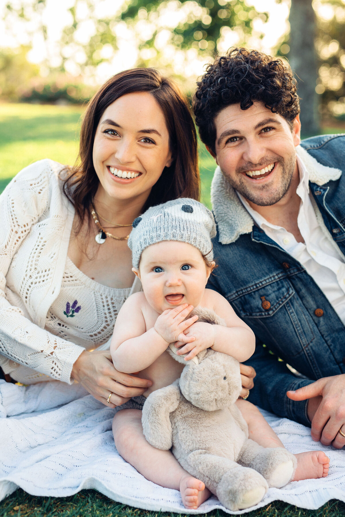 Family Portrait Photo Of Couple Sitting On The Ground With Their Baby Who's Hugging a Stuffed Toy Los Angeles