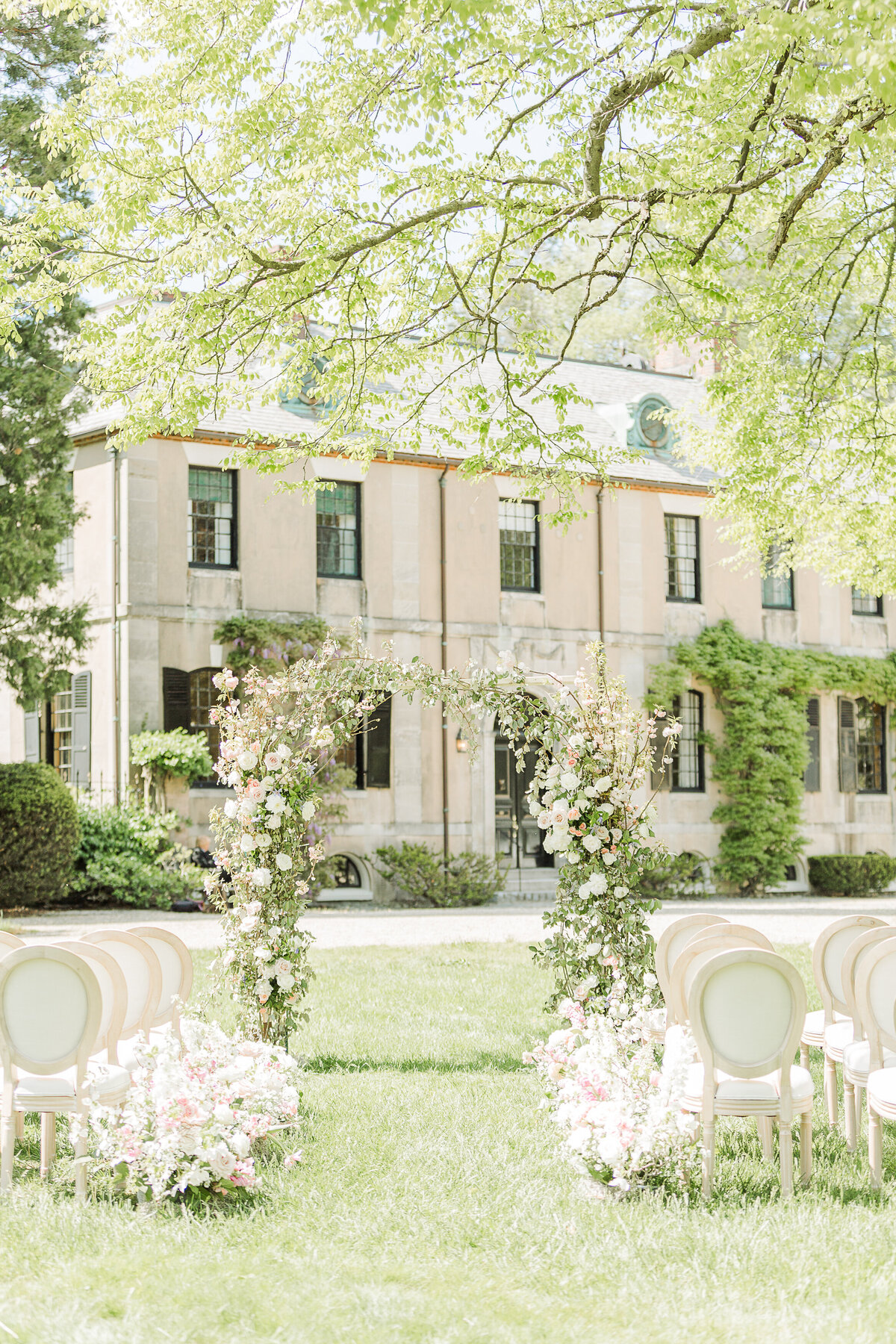 Image of a wedding altar adorned with flowers and greenery with chateau-inspired building on Boston's North Shore. Captured by best Massachusetts wedding photographer Lia Rose Weddings