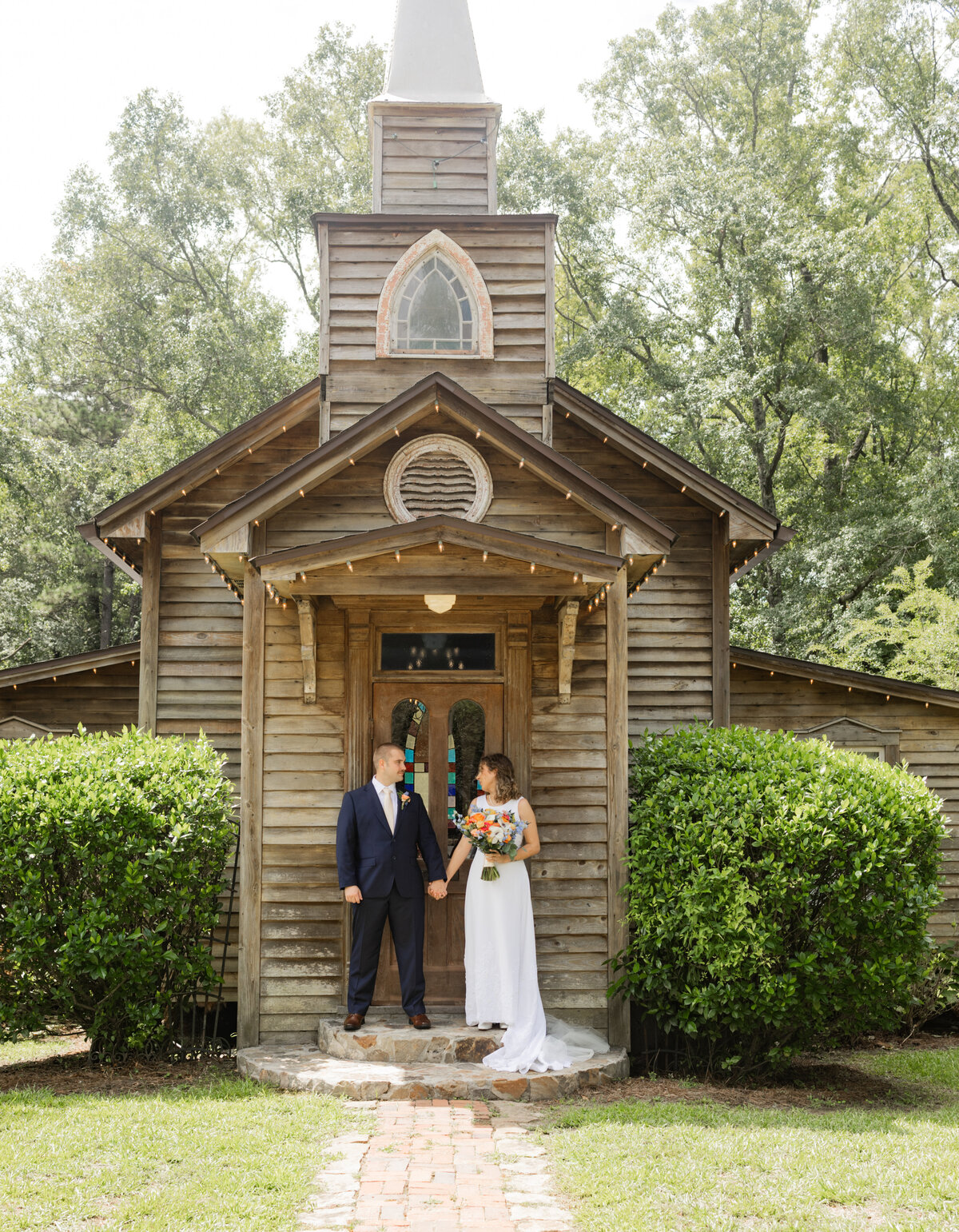 bride and groom holding hands and looking at each other while holding bright colored bouquet at lake pines event center in midland georgia by Amanda Richardson Photography