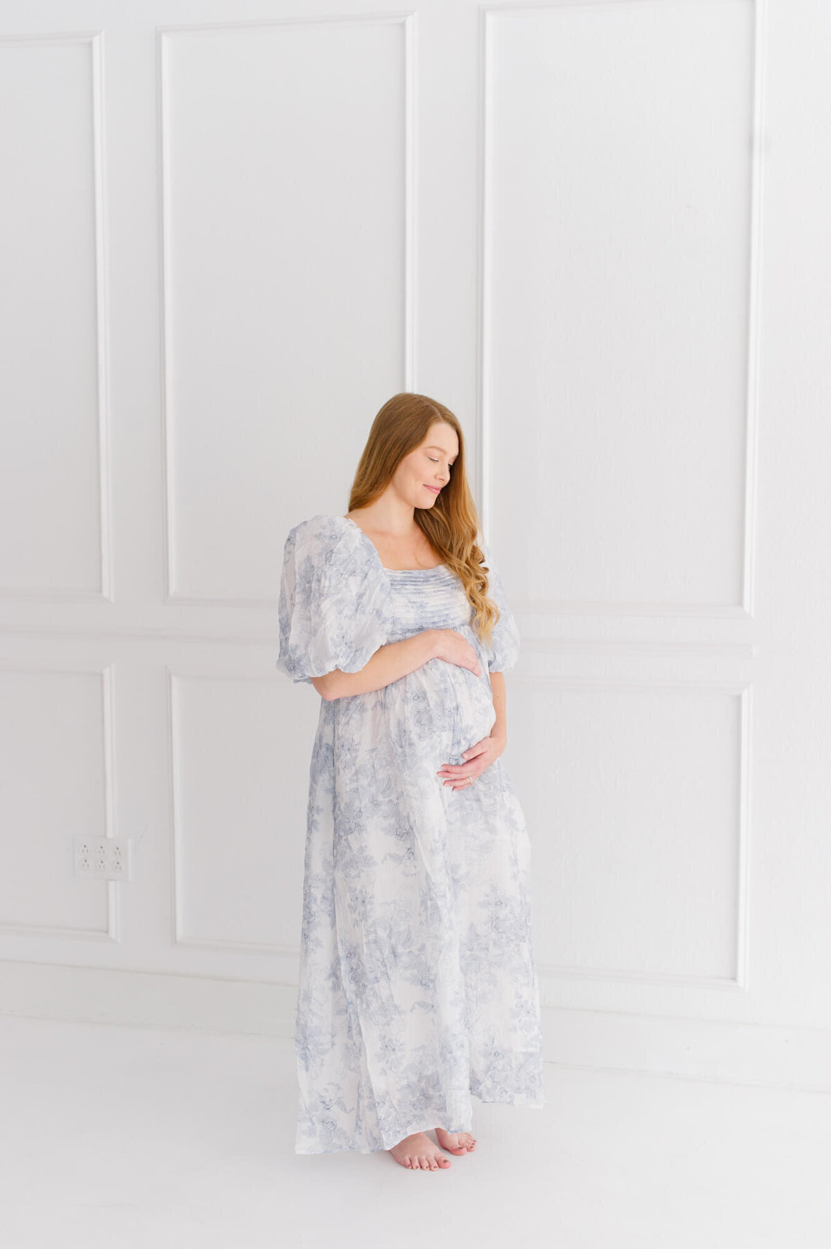Pregnant mom stands in front of beautiful white studio wall while holding her belly