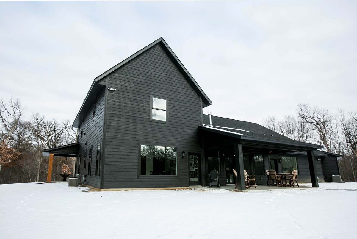 Exterior back view of custom home in Elk River, Minnesota with black siding, wood details and patio built by Cornerstone Custom Builds