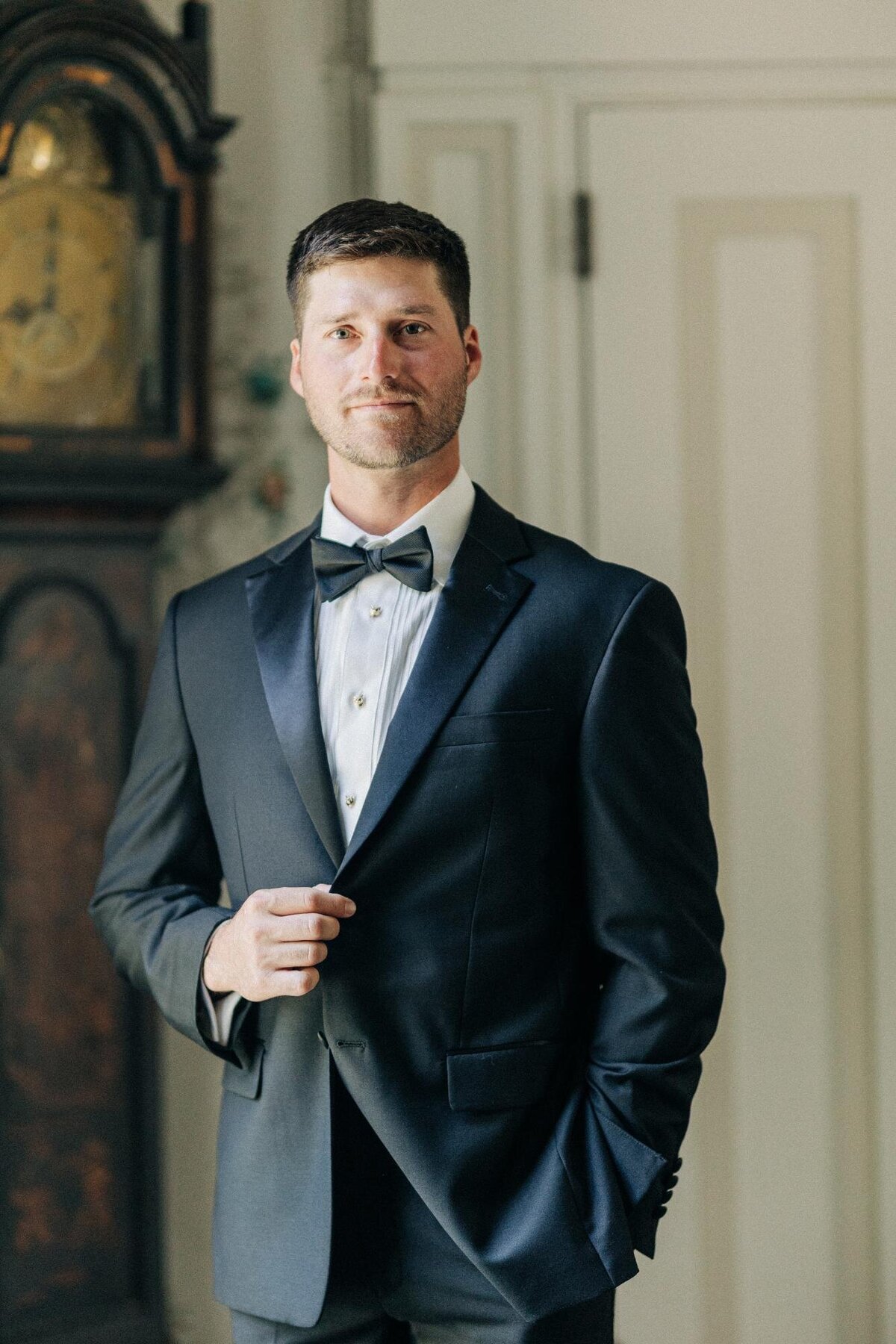A man in a formal black tuxedo and bow tie posing with his hands in his pockets.