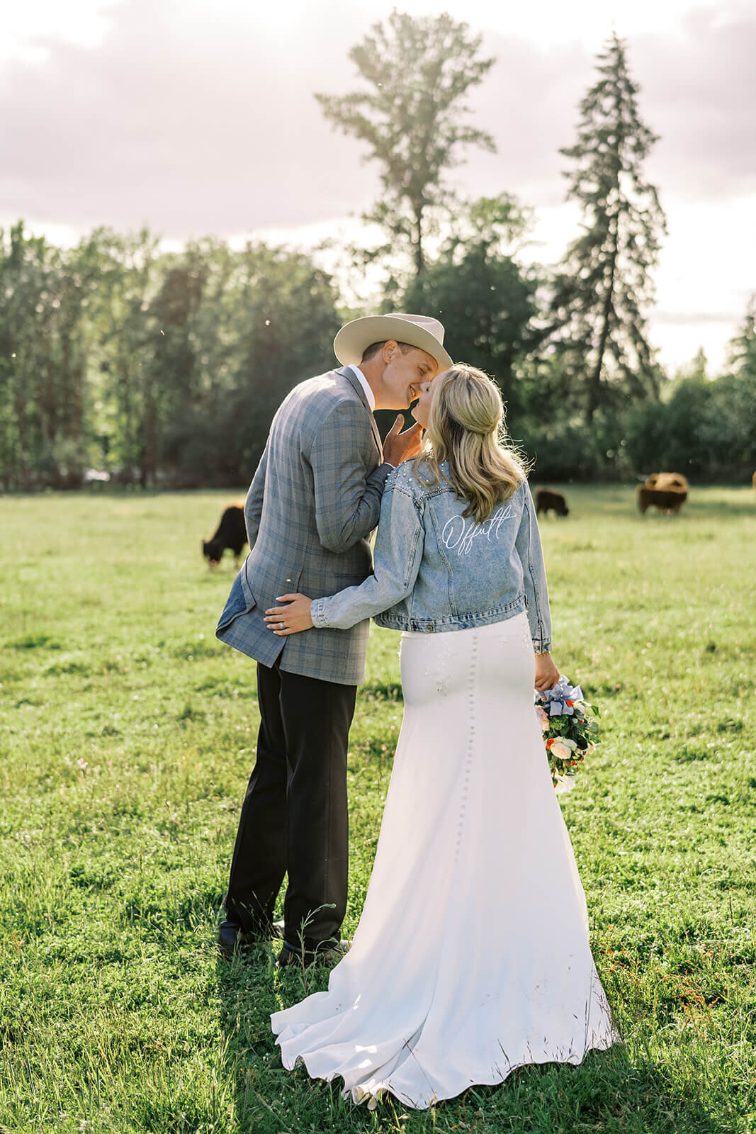 A bride and groom kiss in a field with their backs towards the camera.