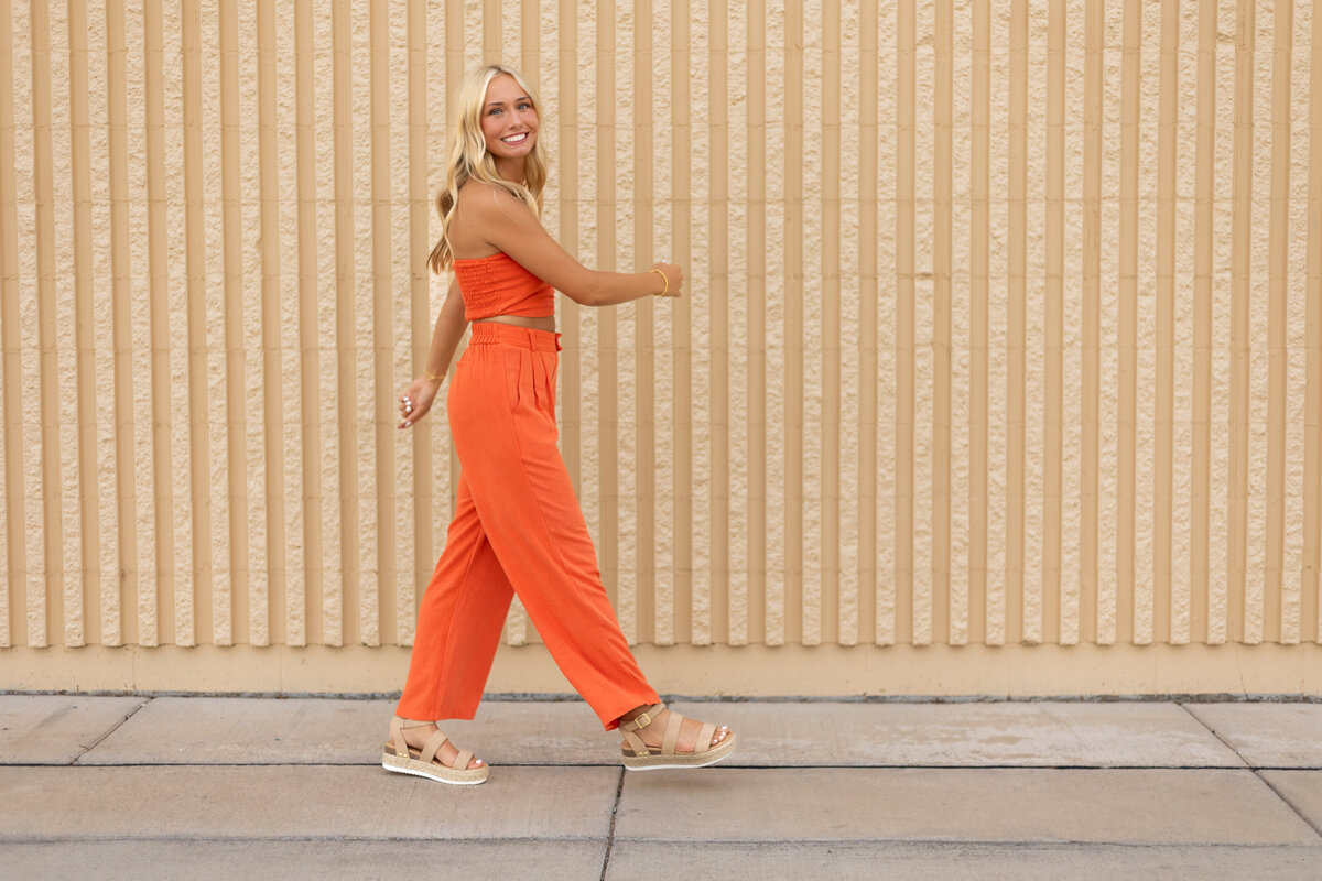 A senior girl in an orange jumpsuit poses on an illuminated staircase at night, creating a cinematic, moody cityscape portrait.