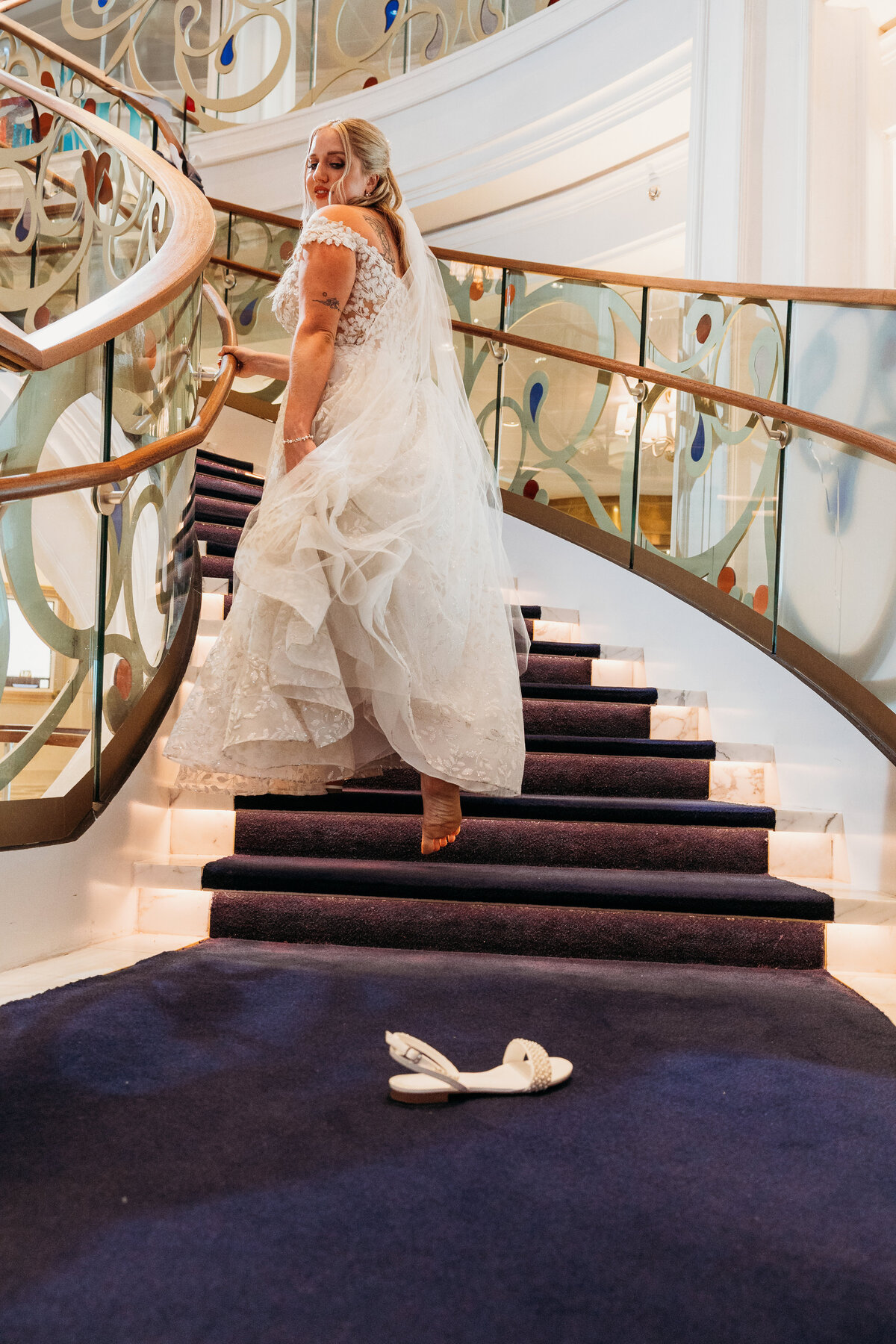 Bride runs barefoot up a staircase on the Disney Wish, leaving behind a white sandal in a playful Cinderella-inspired wedding moment.