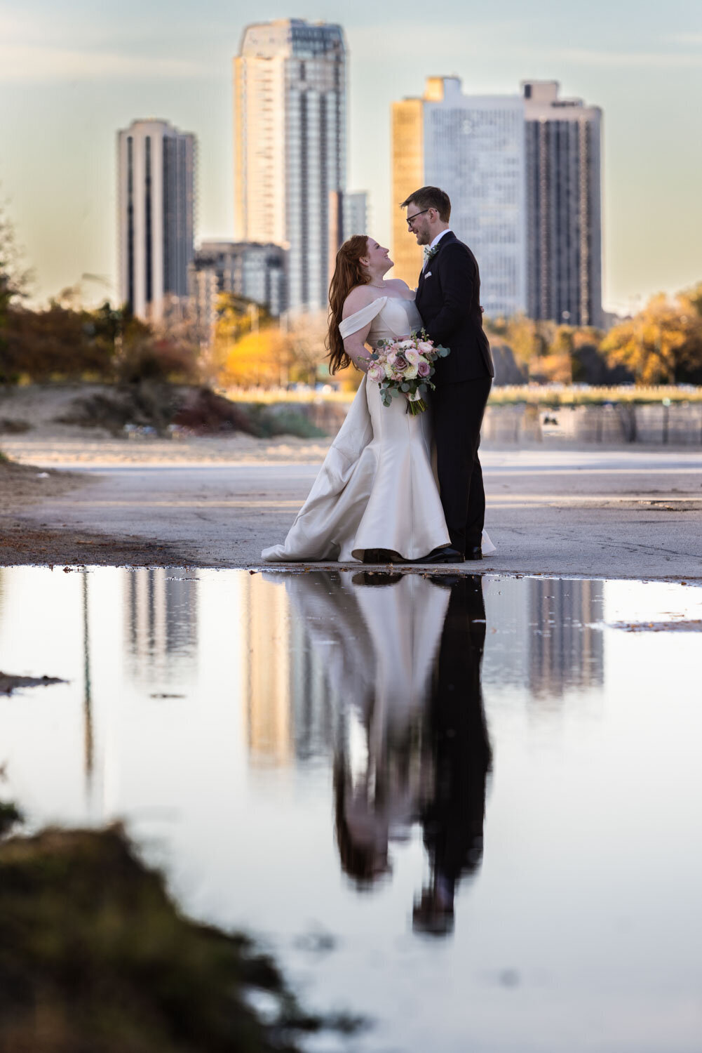 A bride and groom are standing in front of a body of water.
