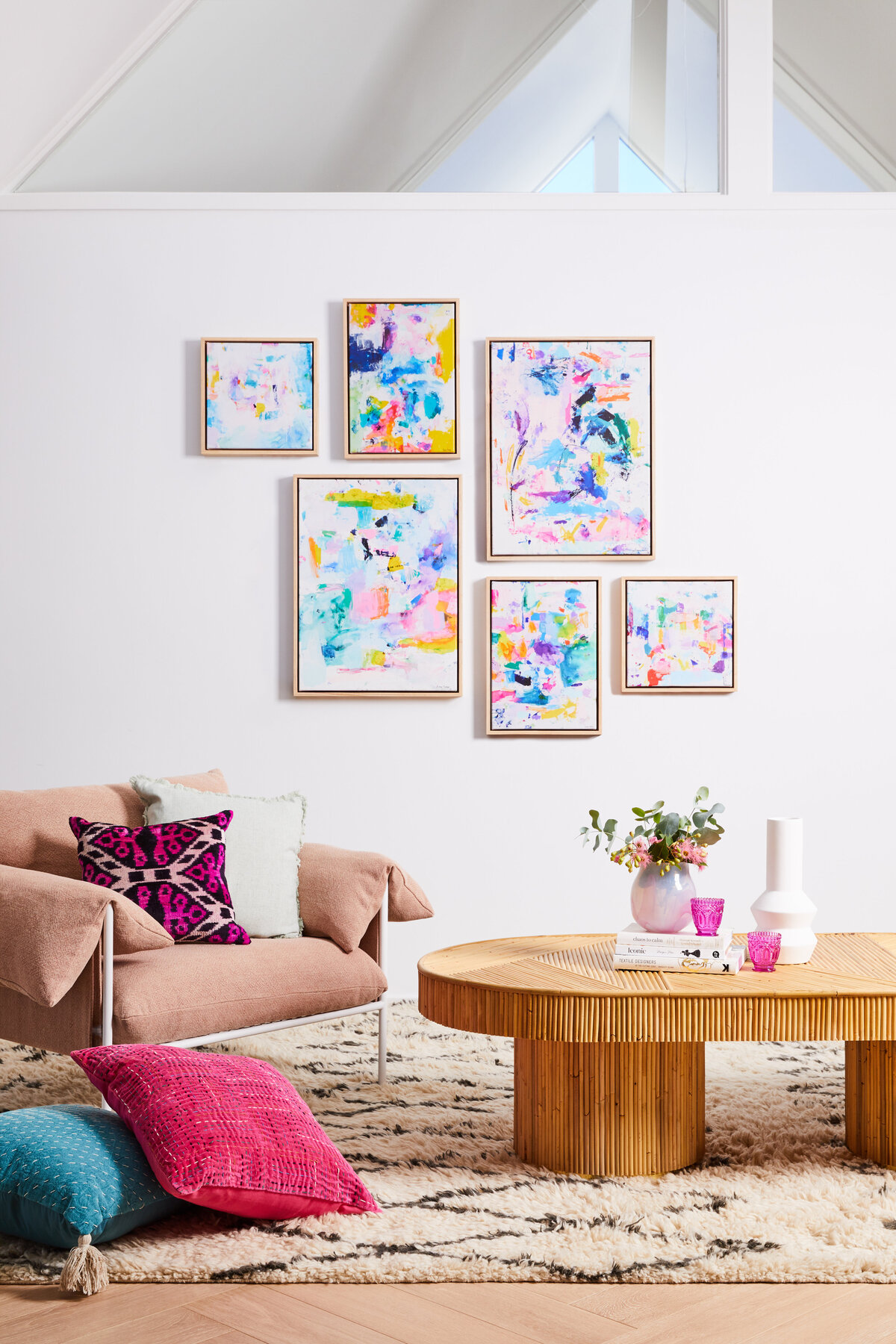 Residential interior design project by interior stylist in Melbourne, showcasing a modern living room with abstract artwork, pink armchair, colorful cushions, and natural wood coffee table. Interior decorator service for Sandringham residential space. 