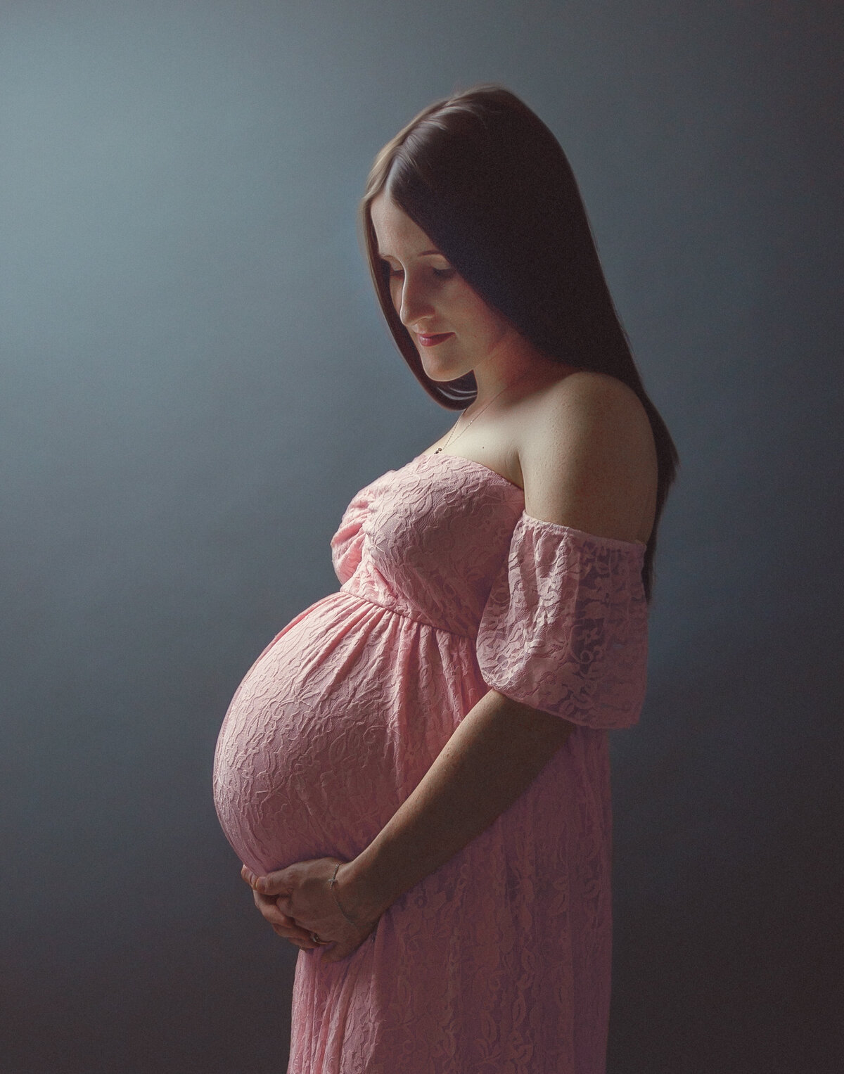 pregnant mother in a long baby pink dress holding her belly with both hands