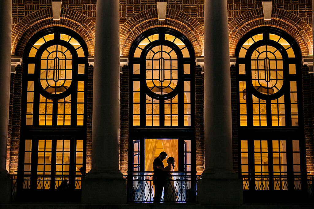 The silhouette of a newlywed couple against massive windows