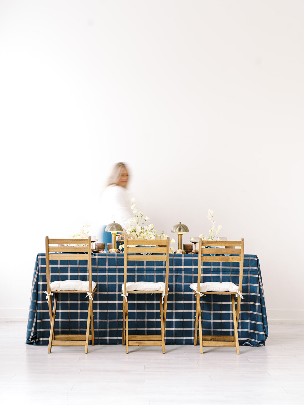 Wedding Planner Kayla of Ascend Events is blurry while walking past a set table at a styled photoshoot for her brand. 
