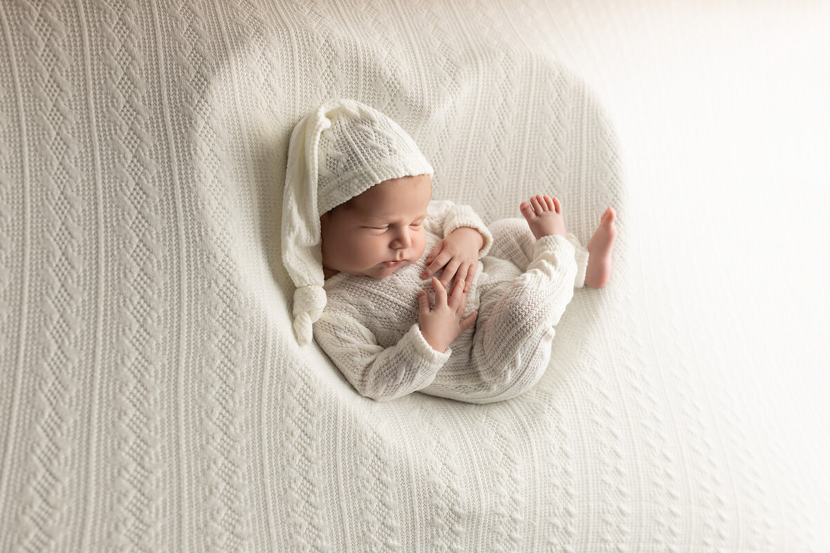 Baby boy in a soft white knit outfit resting peacefully during a fine art newborn session with Dallas luxury photographer