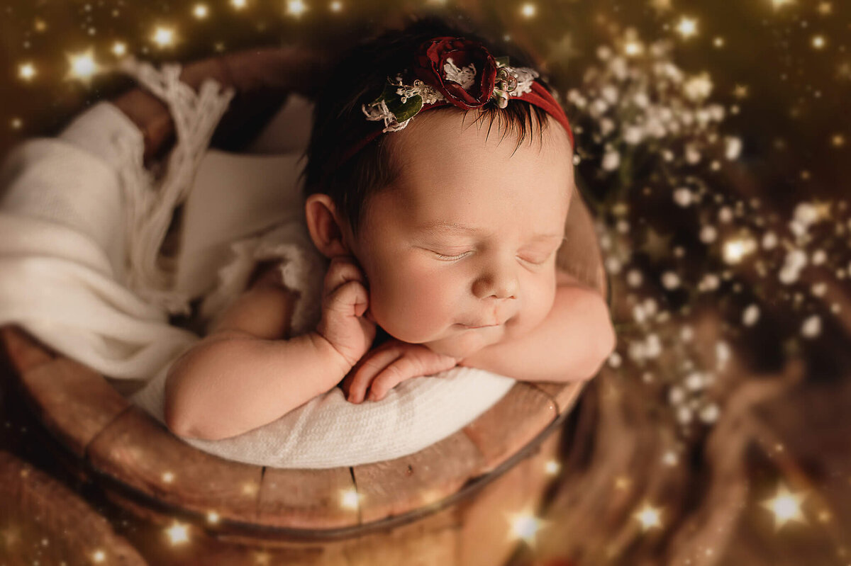 Infant girl sleeping in a wood bucket with hand on her cheek with light leaks.