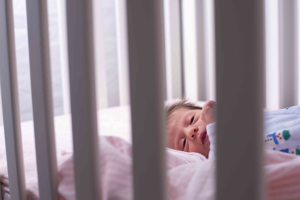 a newborn baby looks through the bars of his crib