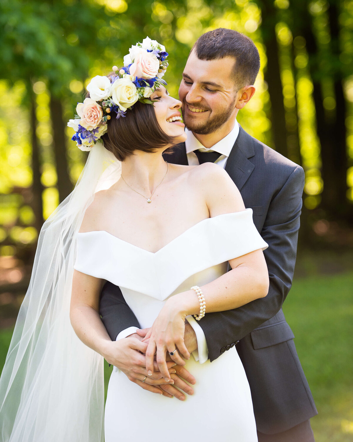 A bride wearing a floral crown is hugged by her groom from behind during their Ottawa wedding photos