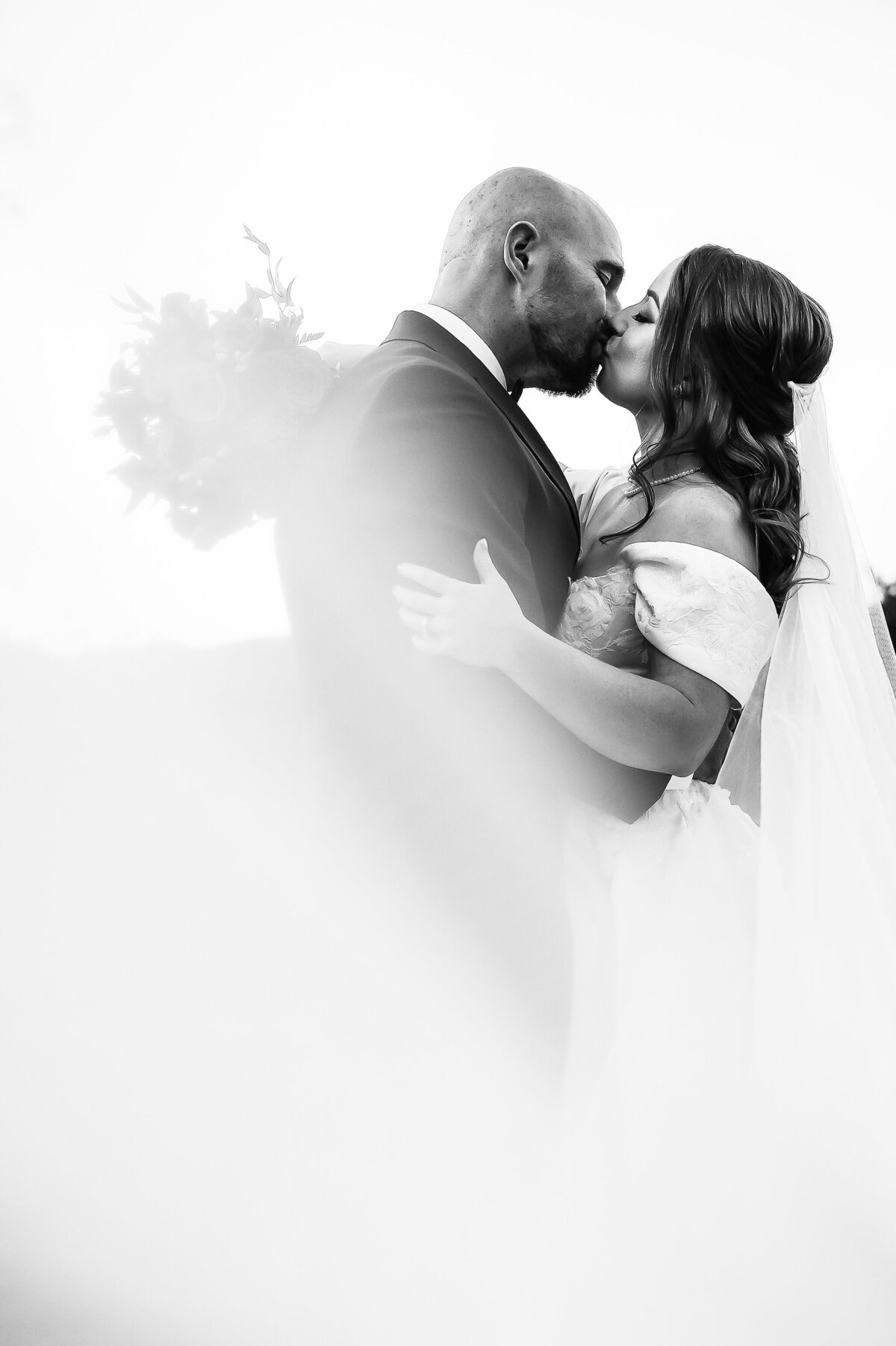 bride and groom kissing as vail swoops around them in black and white photo at Barn on the Pemi wedding in Plymouth NH