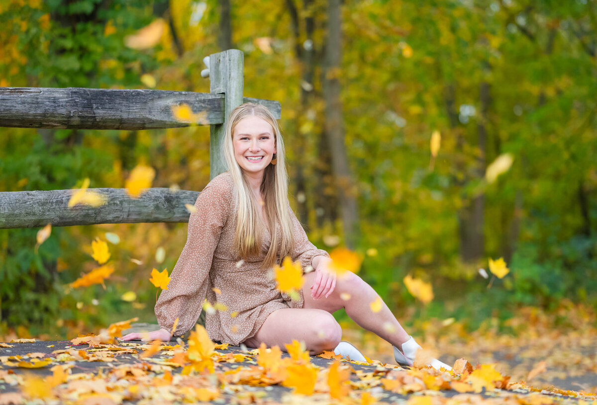 high school senior girl sitting in fall leaves