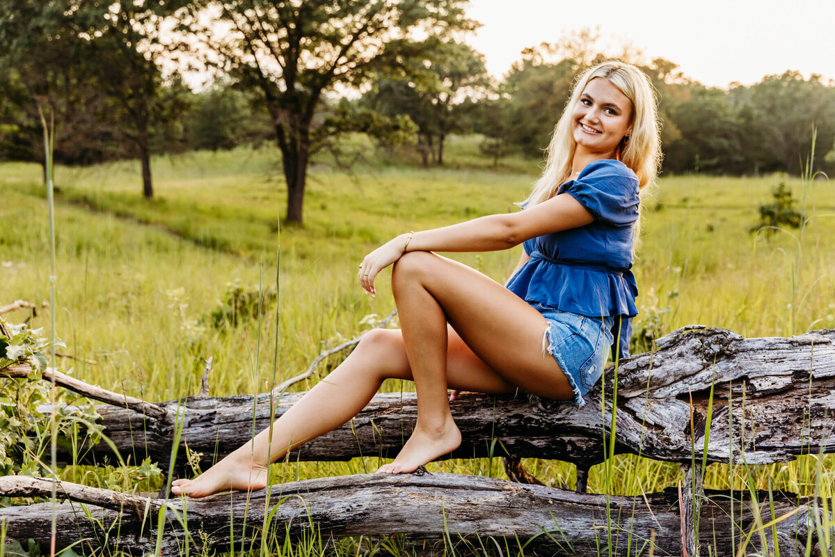 Neenah high school student sitting on top of a fallen tree and resting her hand on her knee as she looks over her shoulder captured by Ashley Kalbus Photography