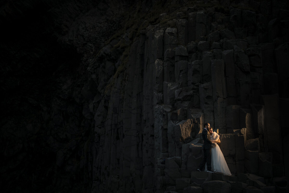 A wedding couple standing on a rock formation lit up by a small lantern.