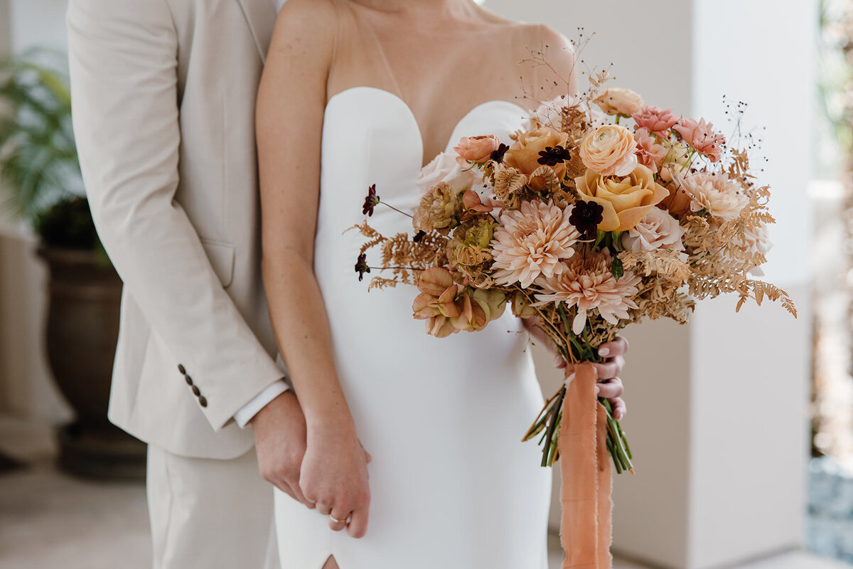 Bride holding a bouquet with peach and brown flowers with peach ribbon