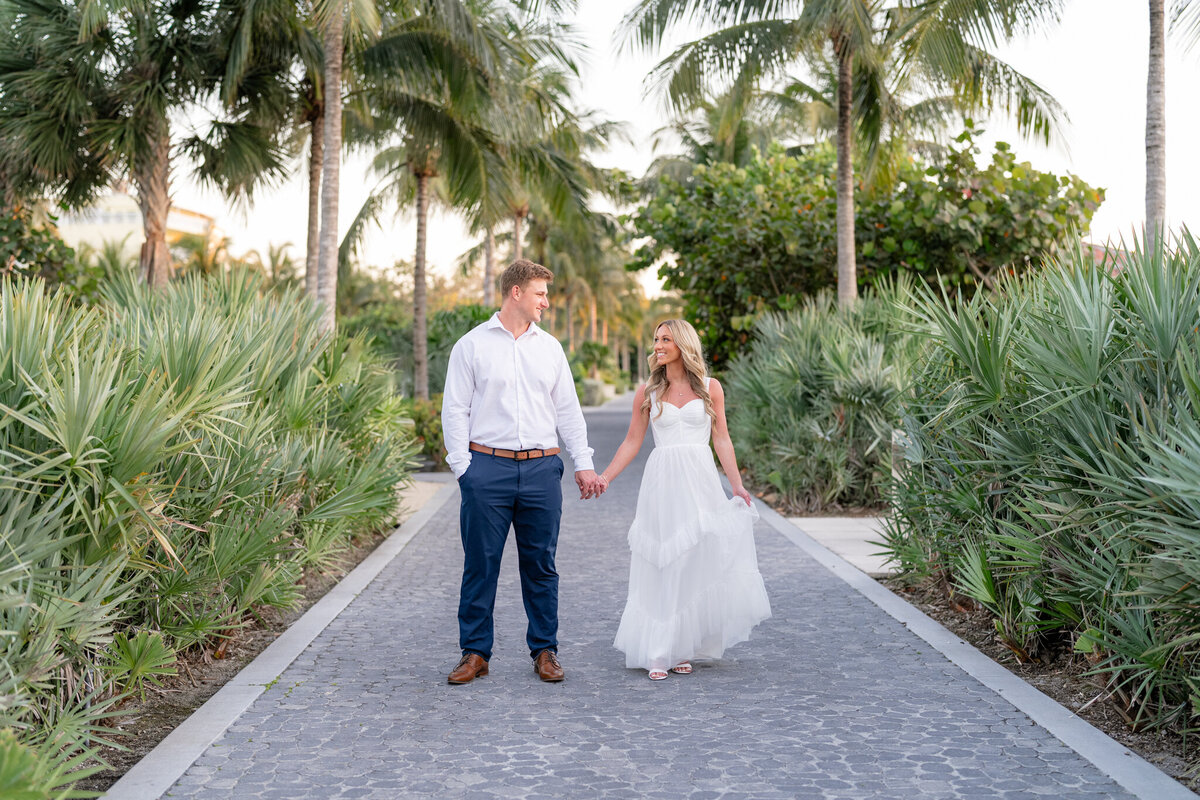 Couple holding hands and standing on path lined with palms and greenery