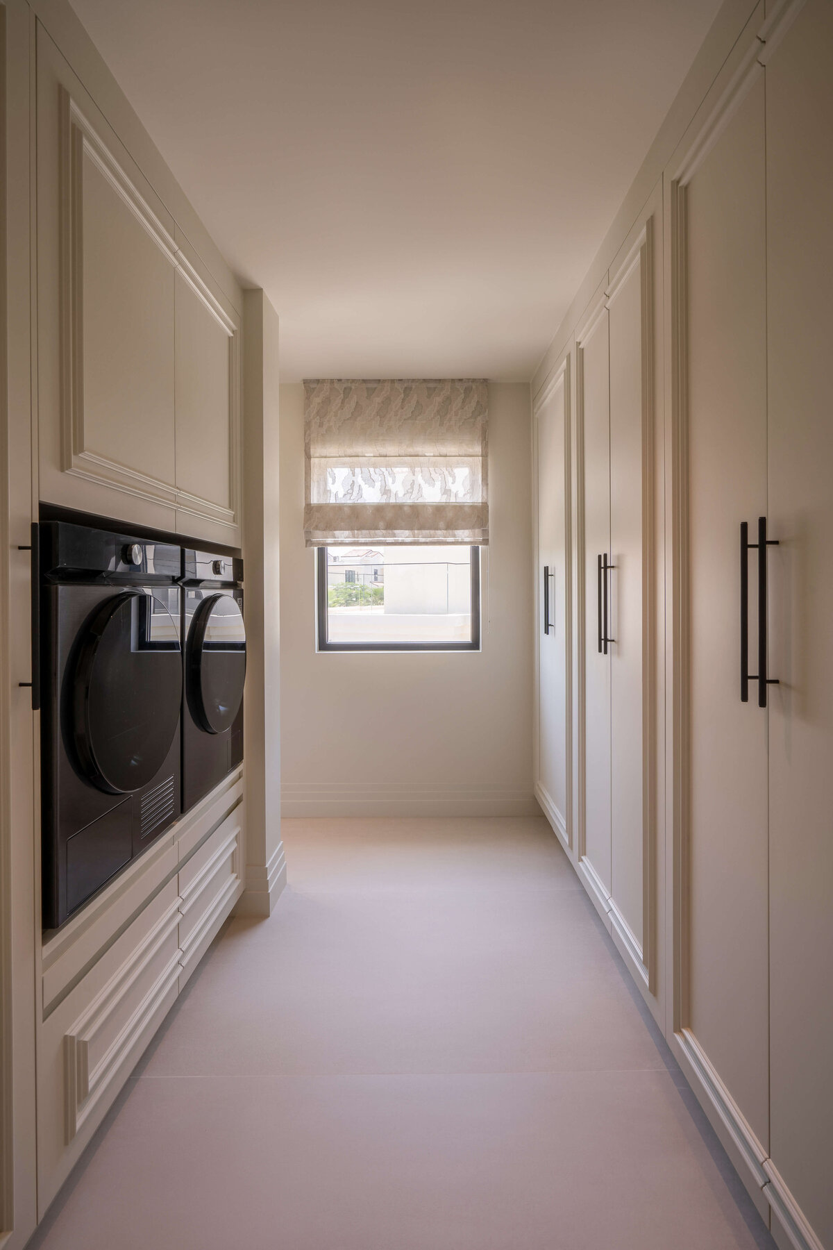 Built-in laundry and storage. The cabinets are neutral white with black hardware. The washer and dryer unit are modern and all-black.