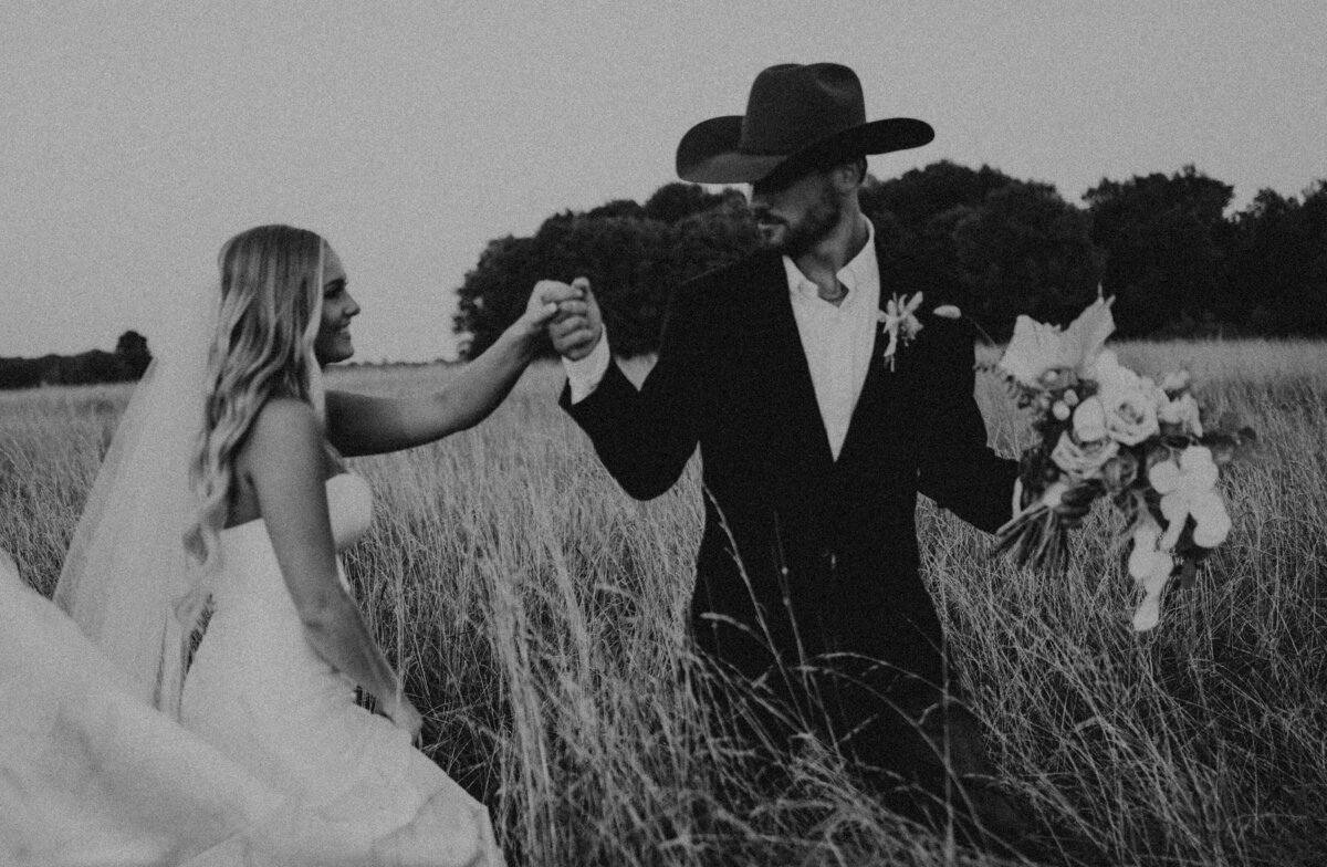 bride and groom walking through a field holding hands