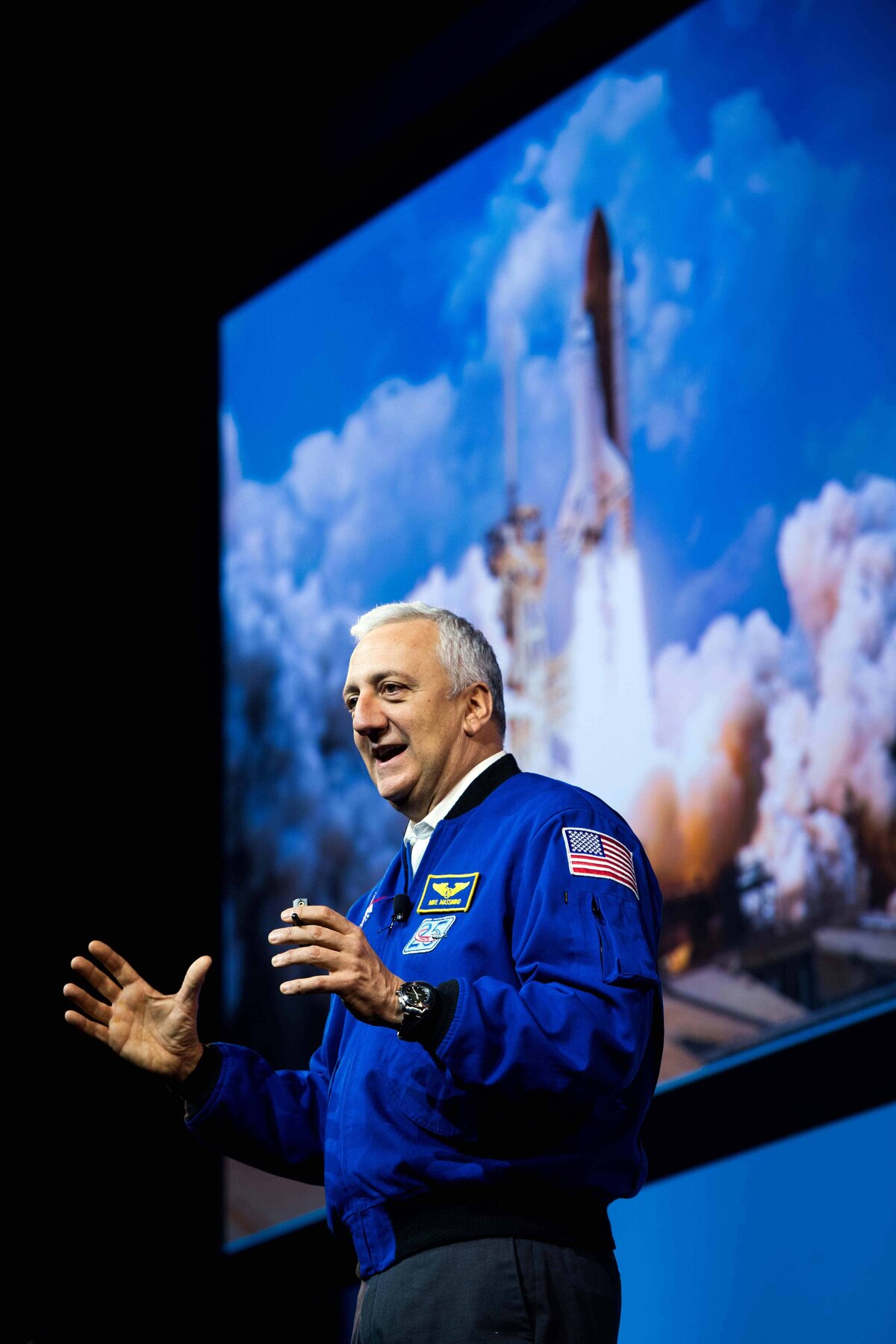 Mike Massimo speaks at conference with image of rocket ship behind him