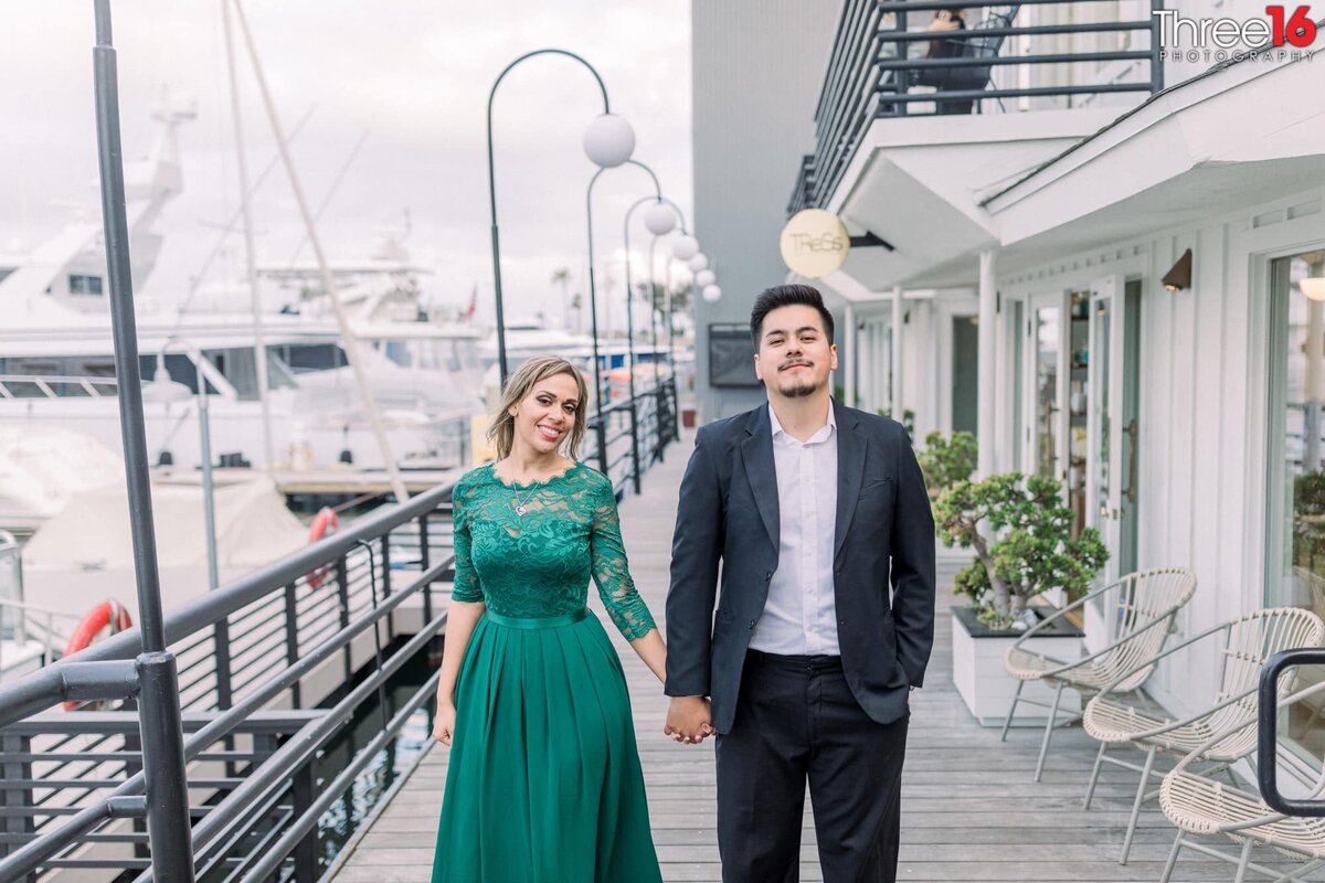 Engaged couple hold hands as they pose for photos at the Lido Marina Village