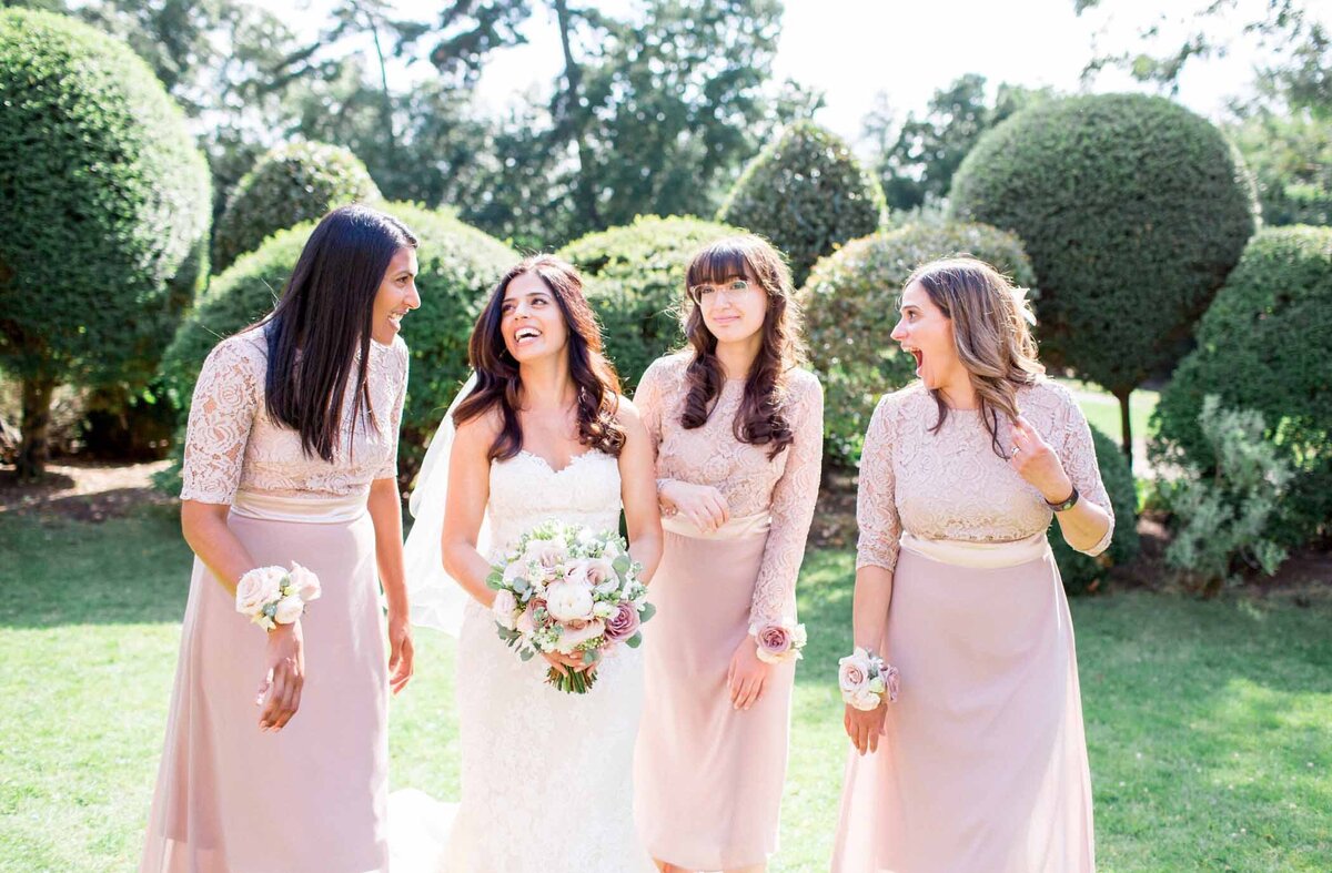 Bride with her bridesmaids laughing on a sunny wedding day at Hampton Court House groom walk up memorial steps at their DC wedding