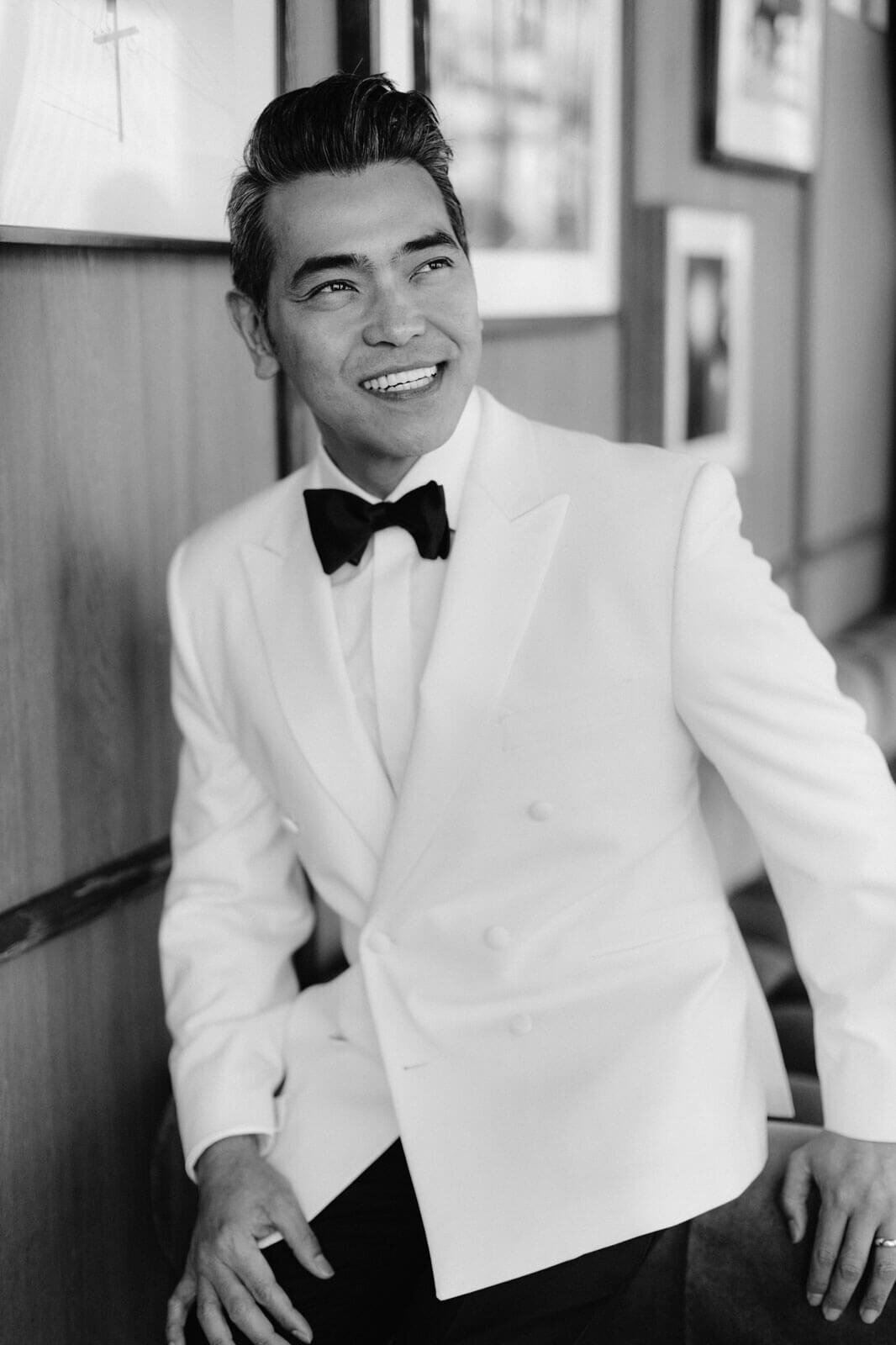 The groom, wearing a white suit, is smiling in The Skylark, New York. Wedding Image by Jenny Fu Studio
