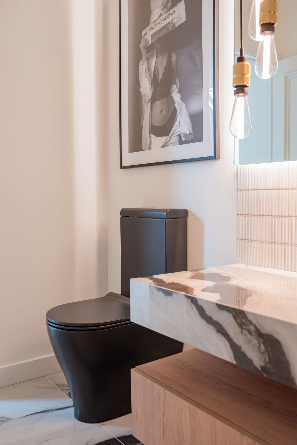 Modern bathroom with marble countertops featuring black veining. A modern matte black sink sits in the left corner with a black and white framed portrait above it.