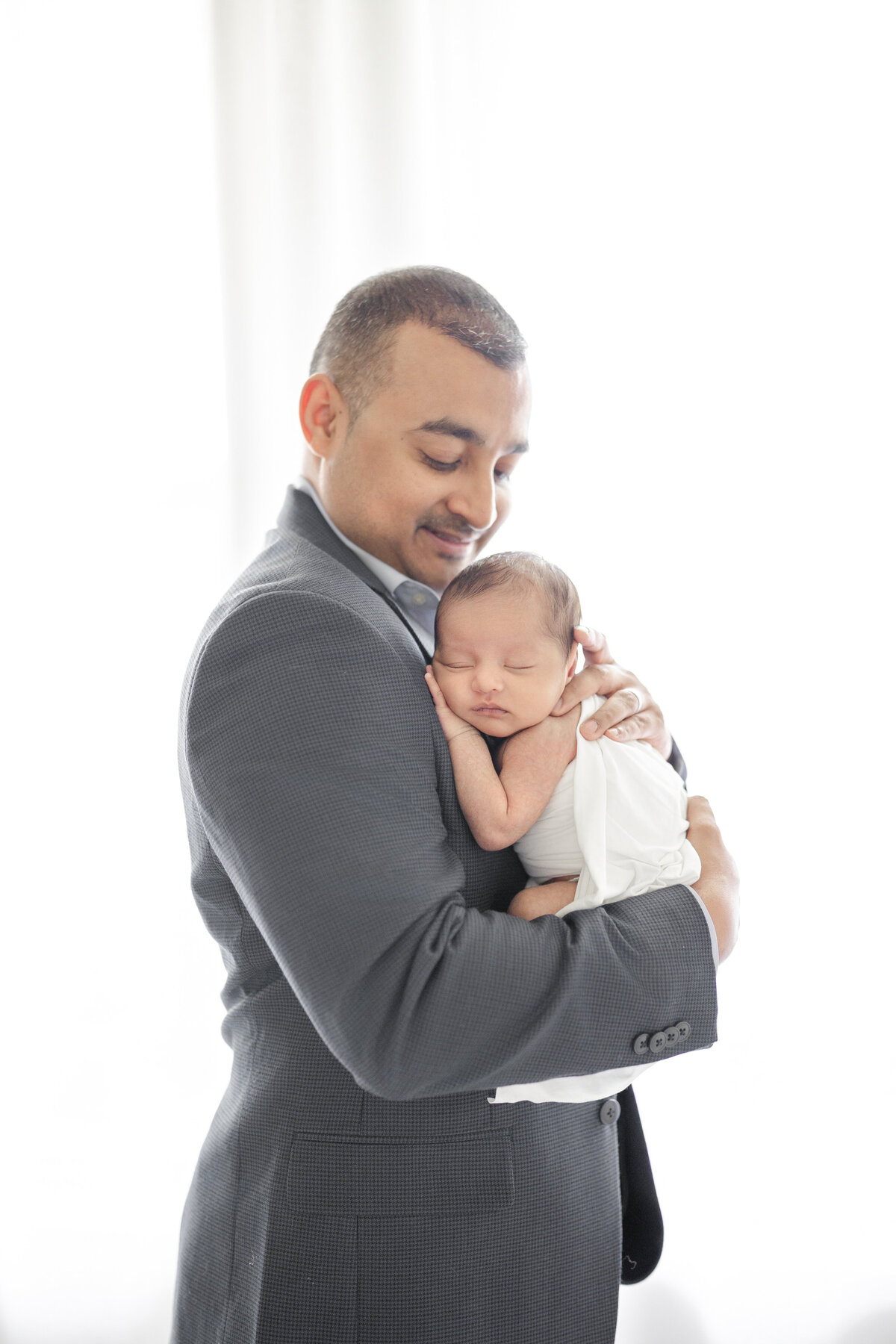 Newborn baby in father’s arms during intimate neutral-toned session at Tampa luxury studio