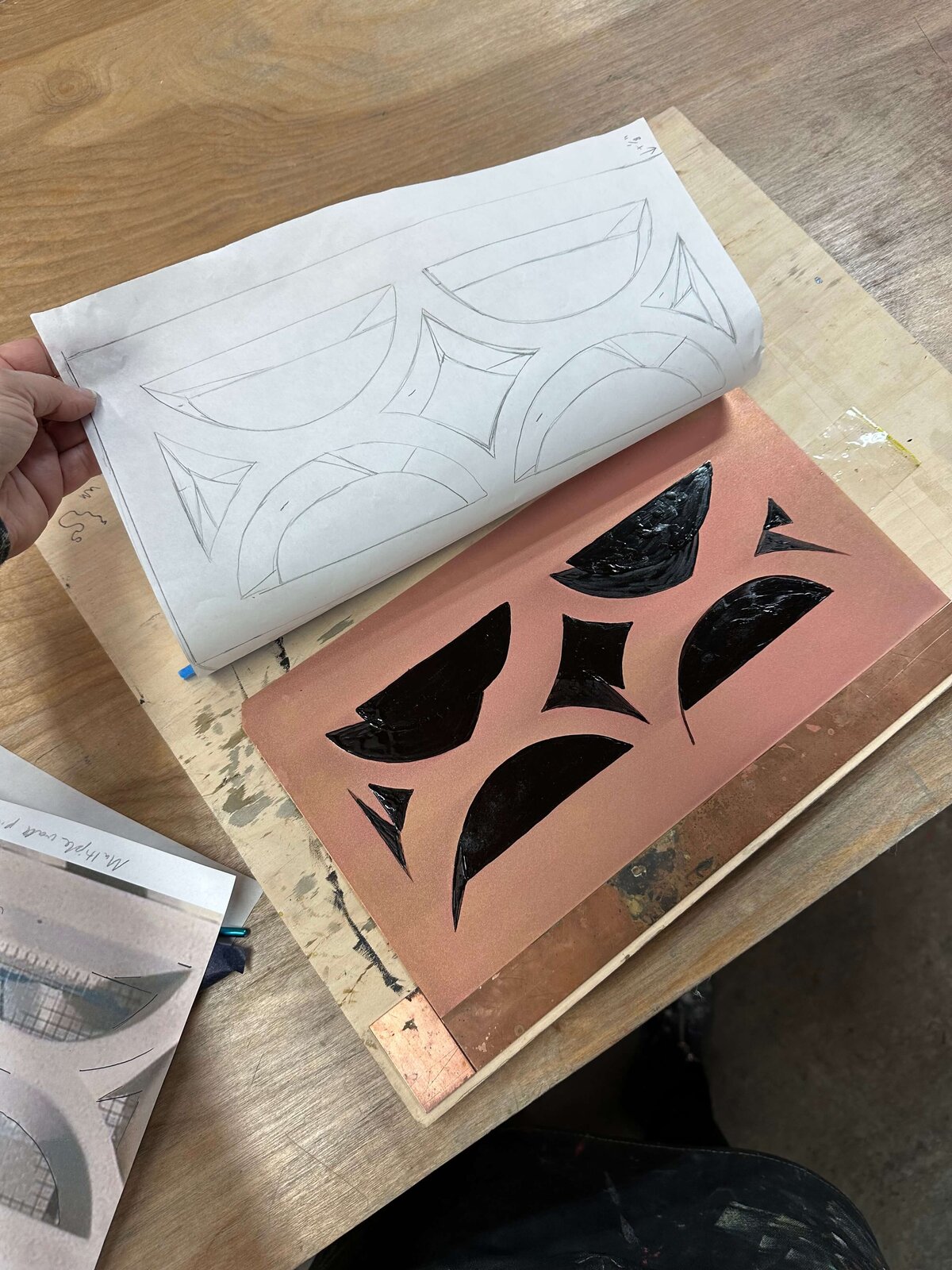 A traced sketch aligned next to a copper plate with matching asphaltum-painted black shapes, showing the design transfer process in step etching.