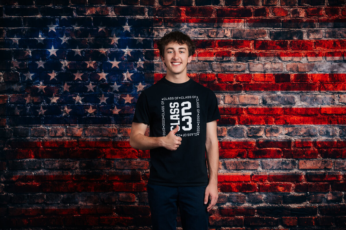 Young man poses against brick wall with flag for Prescott senior photos