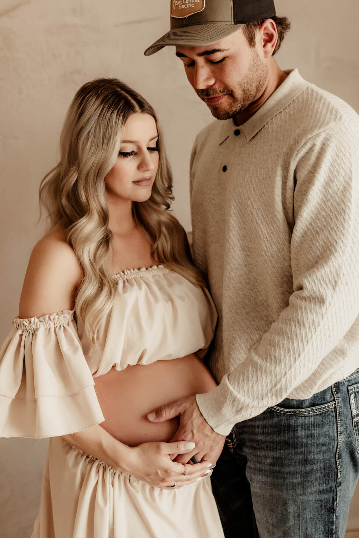 Husband and wife standing next to one antoehr and holding the mother's pregnant belly for a portriait.