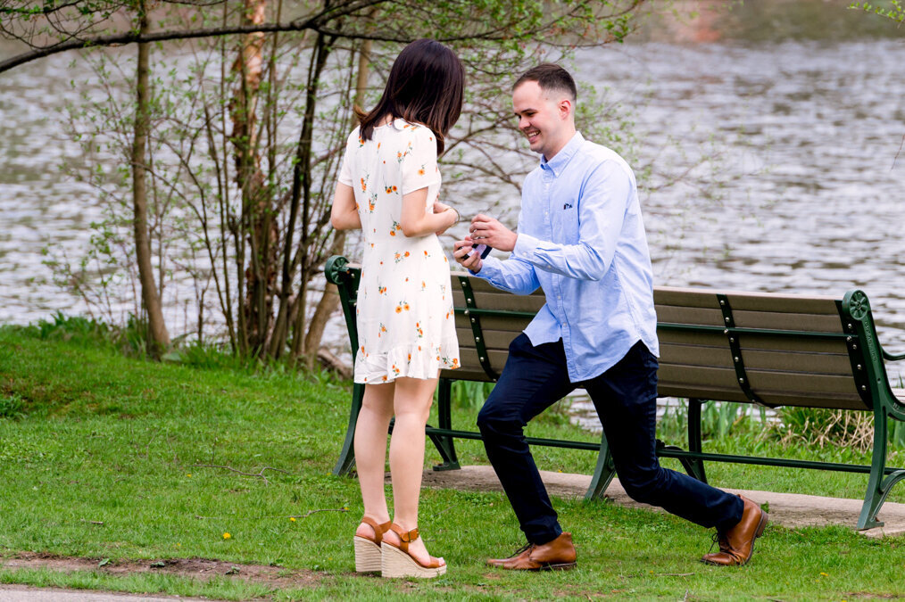 A man proposing to a woman in a park near a pond.