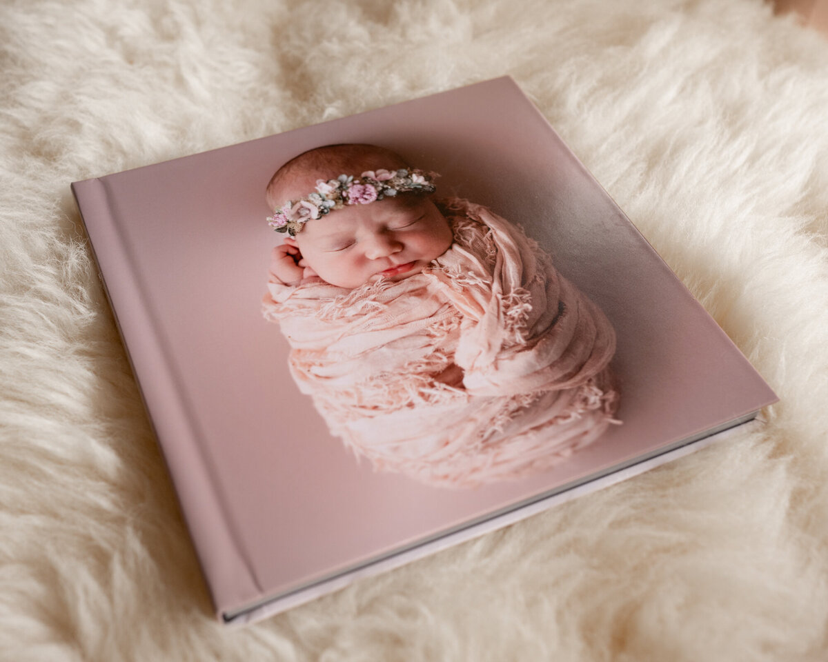 A pink newborn portrait album laying on fur blanket